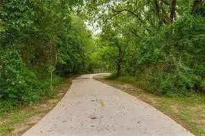 access to Bob Eden Park from the community with Paved pathway bordered by abundant mature trees and dense foliage