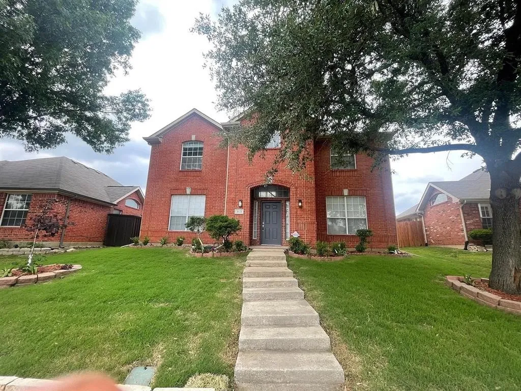 Red brick exterior featuring an arched entryway, multiple windows, a concrete walkway, and landscaped garden beds