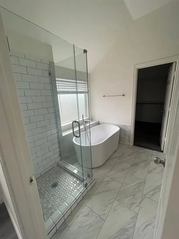 Glass-enclosed shower with subway tile surround and hexagonal tile flooring, freestanding soaking tub, and large format floor tiling