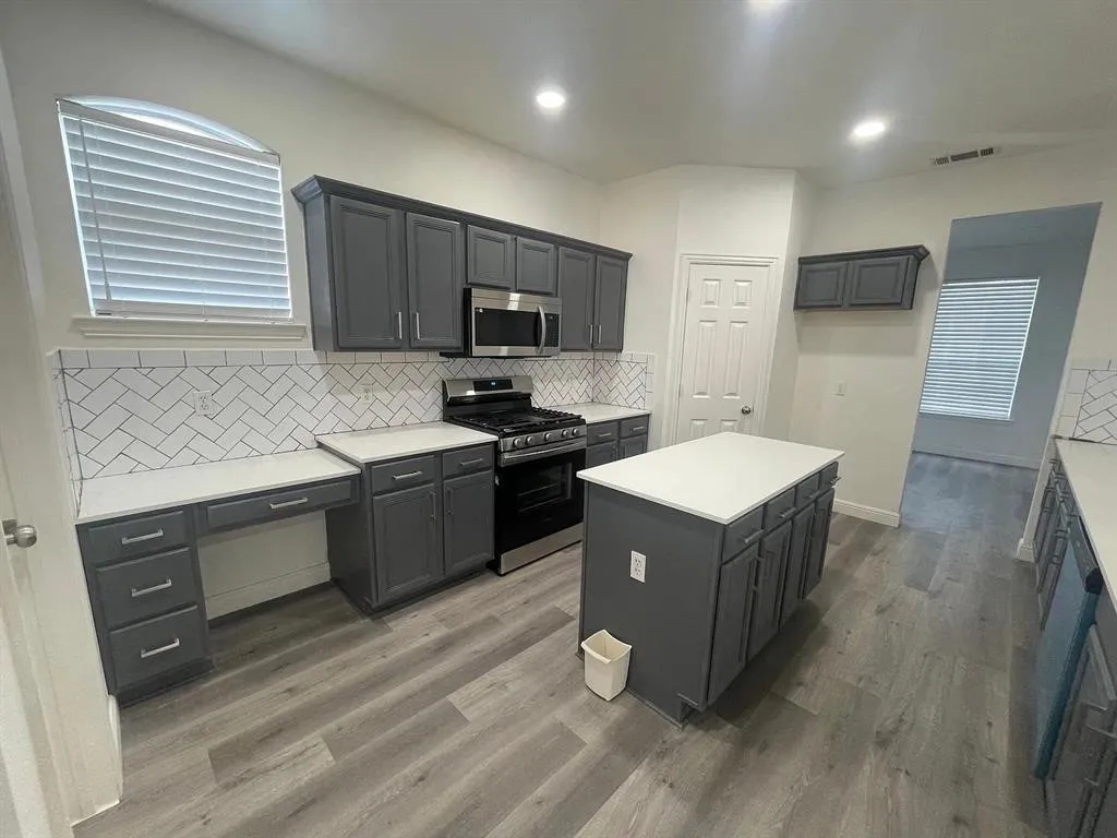 Kitchen featuring a center island, stainless steel appliances, wood-finish flooring, white countertops, and a herringbone tile backsplash