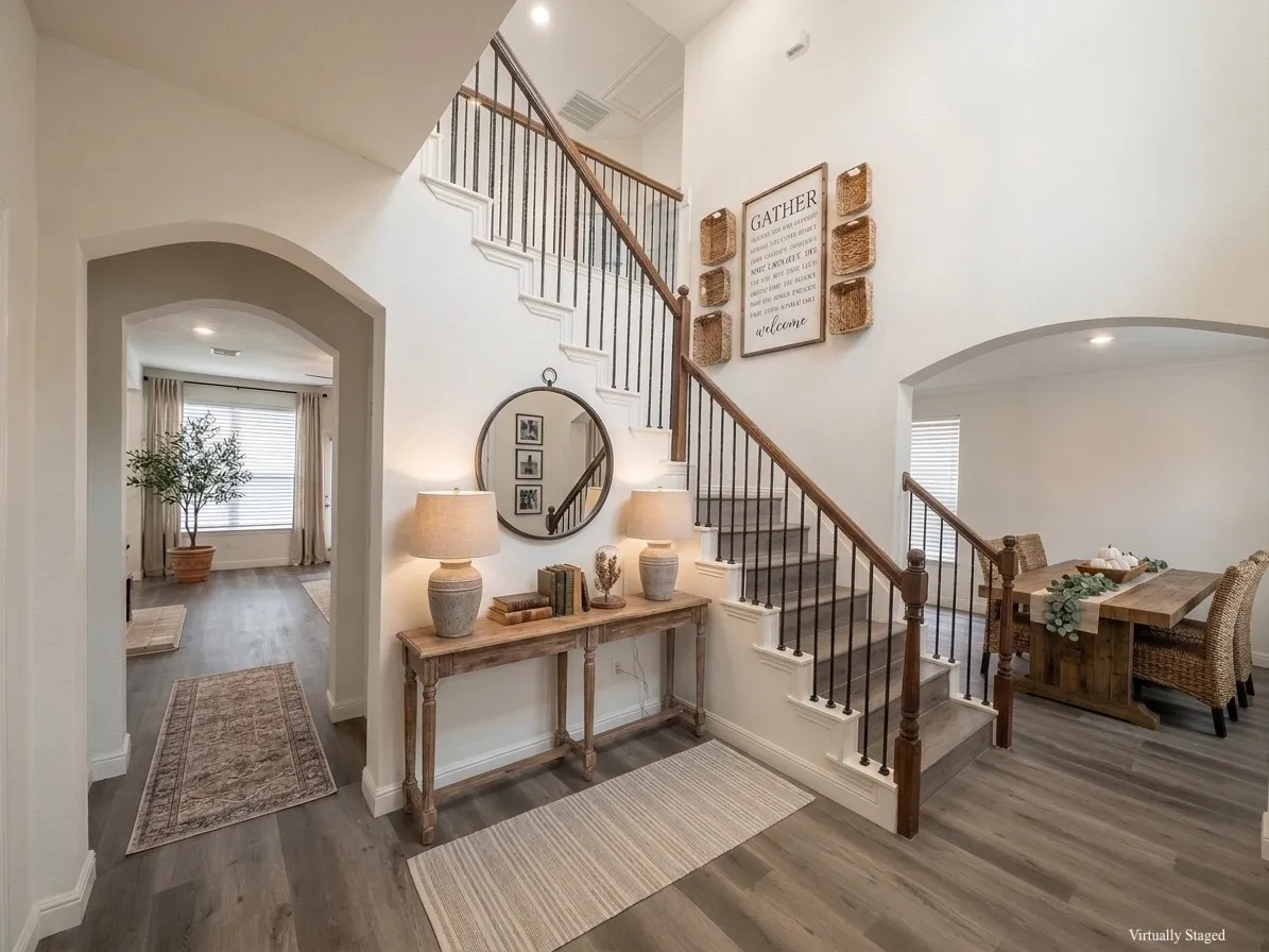 Two-story entryway featuring wood-finish flooring, an arched doorway, and a prominent staircase with dark wood railings and black iron balusters - VIRTUALLY STAGED