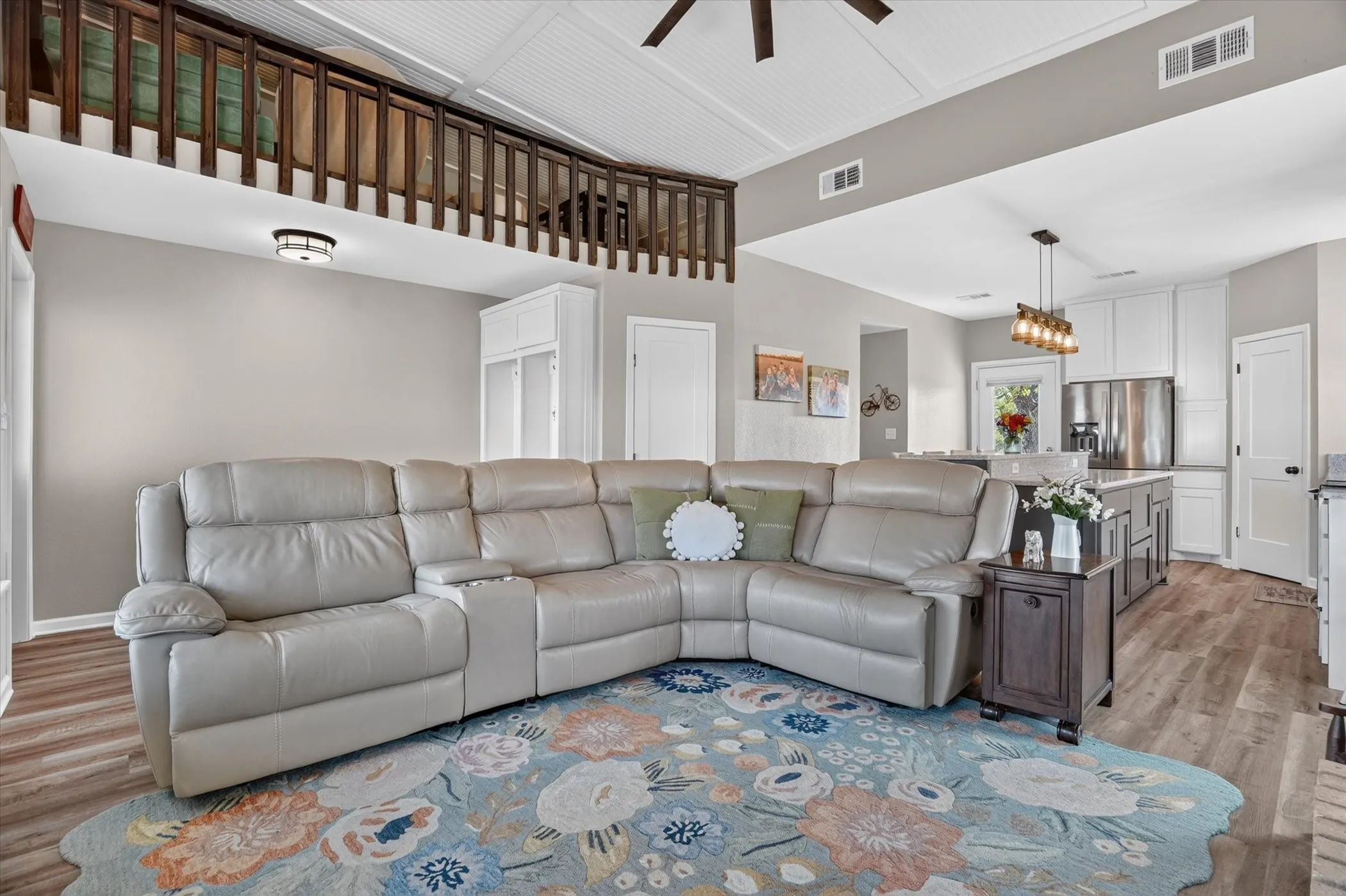 Open-concept living space featuring wood-finish flooring, a wood-railed loft area, and a kitchen with white cabinetry, a center island, and stainless steel appliances