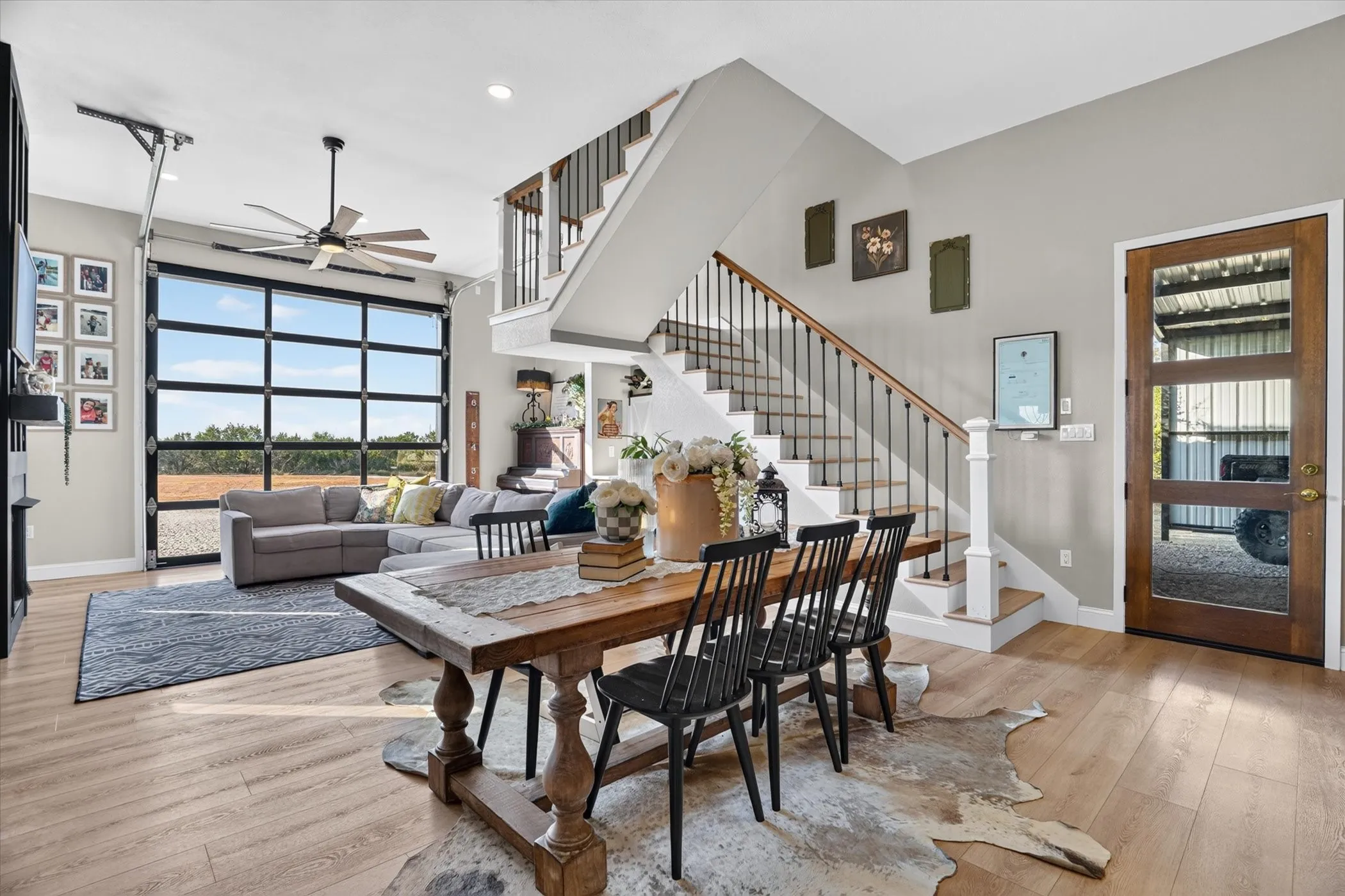 Spacious open-concept living area featuring wood-finish flooring, a modern ceiling fan, and a prominent glass panel door