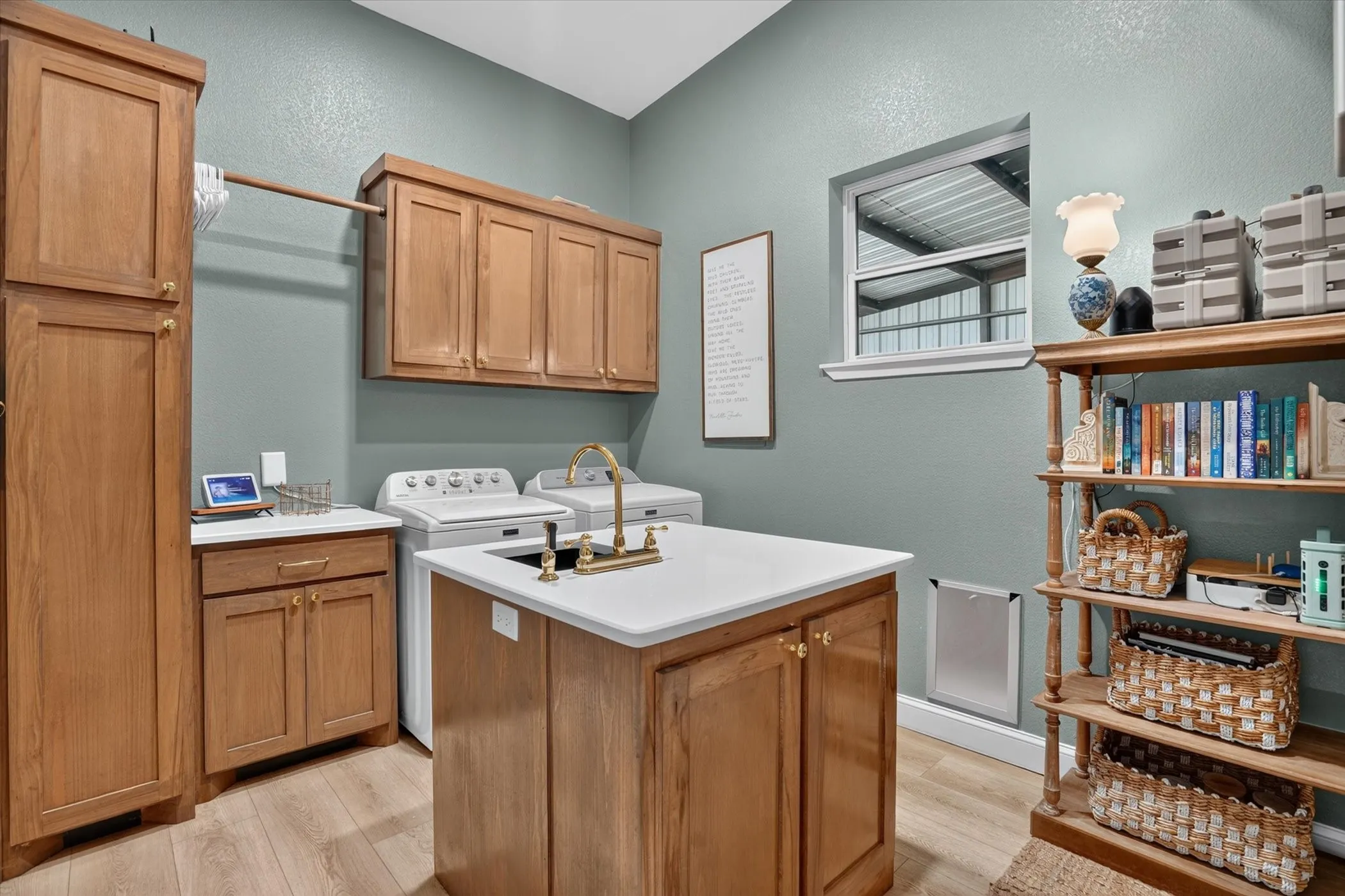 Laundry room featuring an island with an integrated sink and brass-finish faucet, wood-finish cabinetry, light-toned countertops, and wood-finish flooring