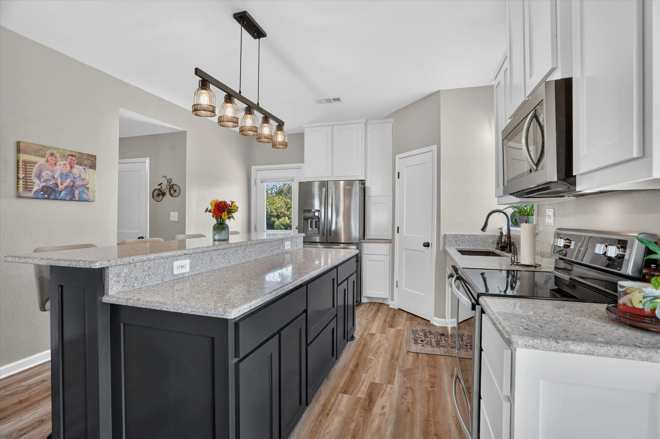 Spacious kitchen with a large island, light-toned countertops, wood-finish flooring, white cabinetry, and stainless steel appliances