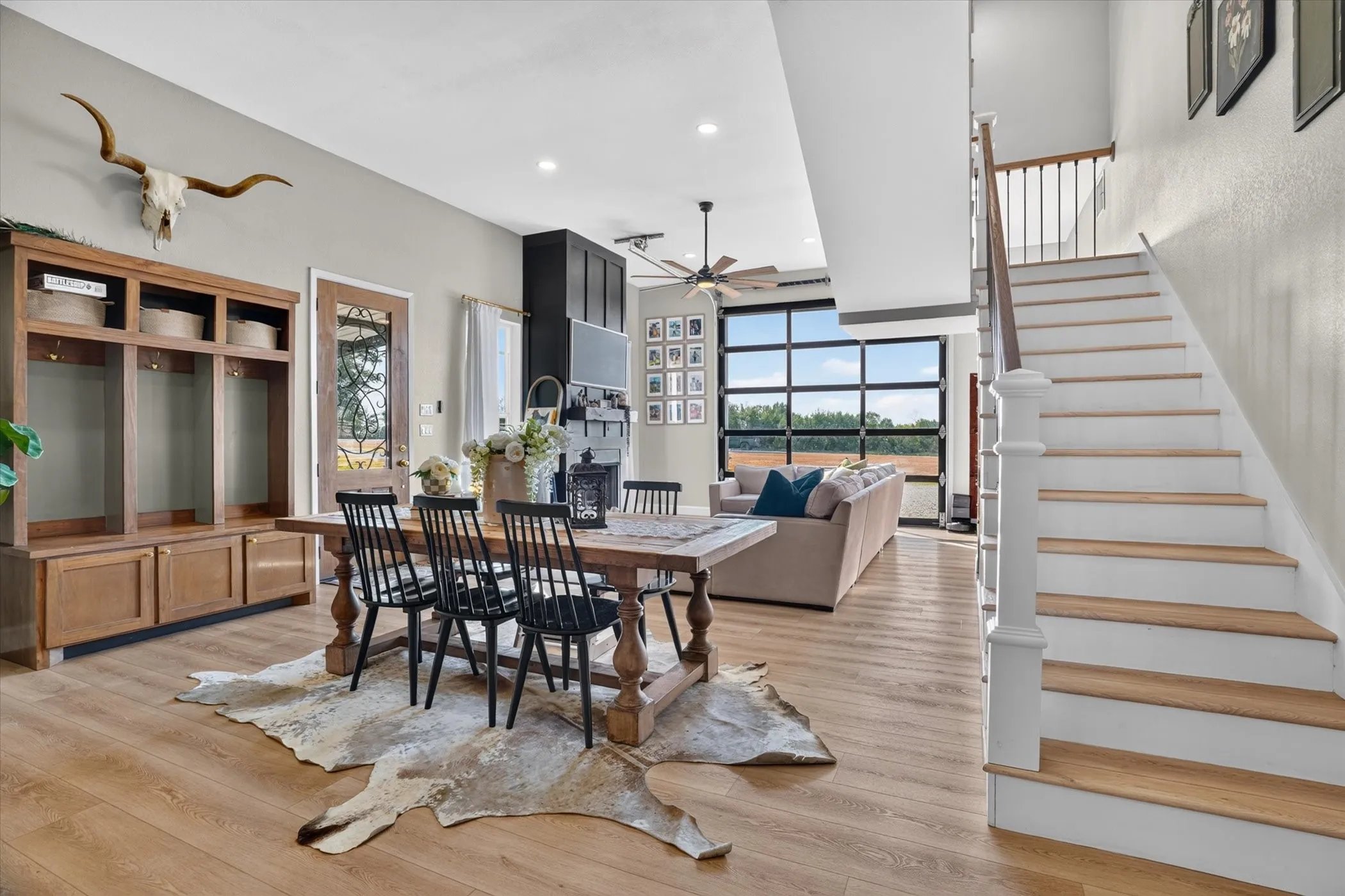 Open-concept living area featuring wood-finish flooring, a full-lite glass garage door, a built-in storage unit, and a painted wood staircase with a metal balustrade