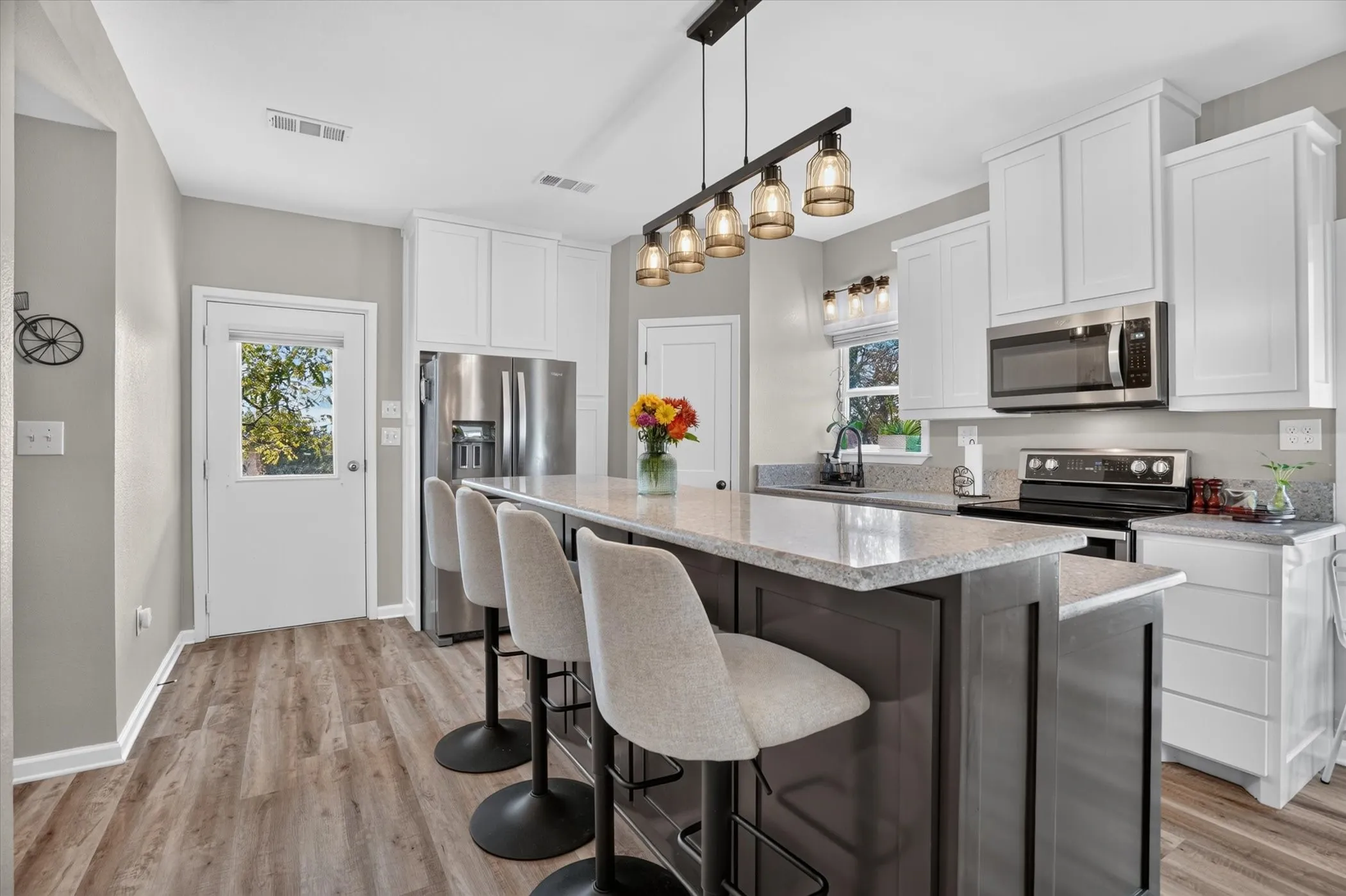 Kitchen featuring wood-finish flooring, two-tone cabinetry, stainless steel appliances, a multi-light pendant fixture, and a center island with countertop seating