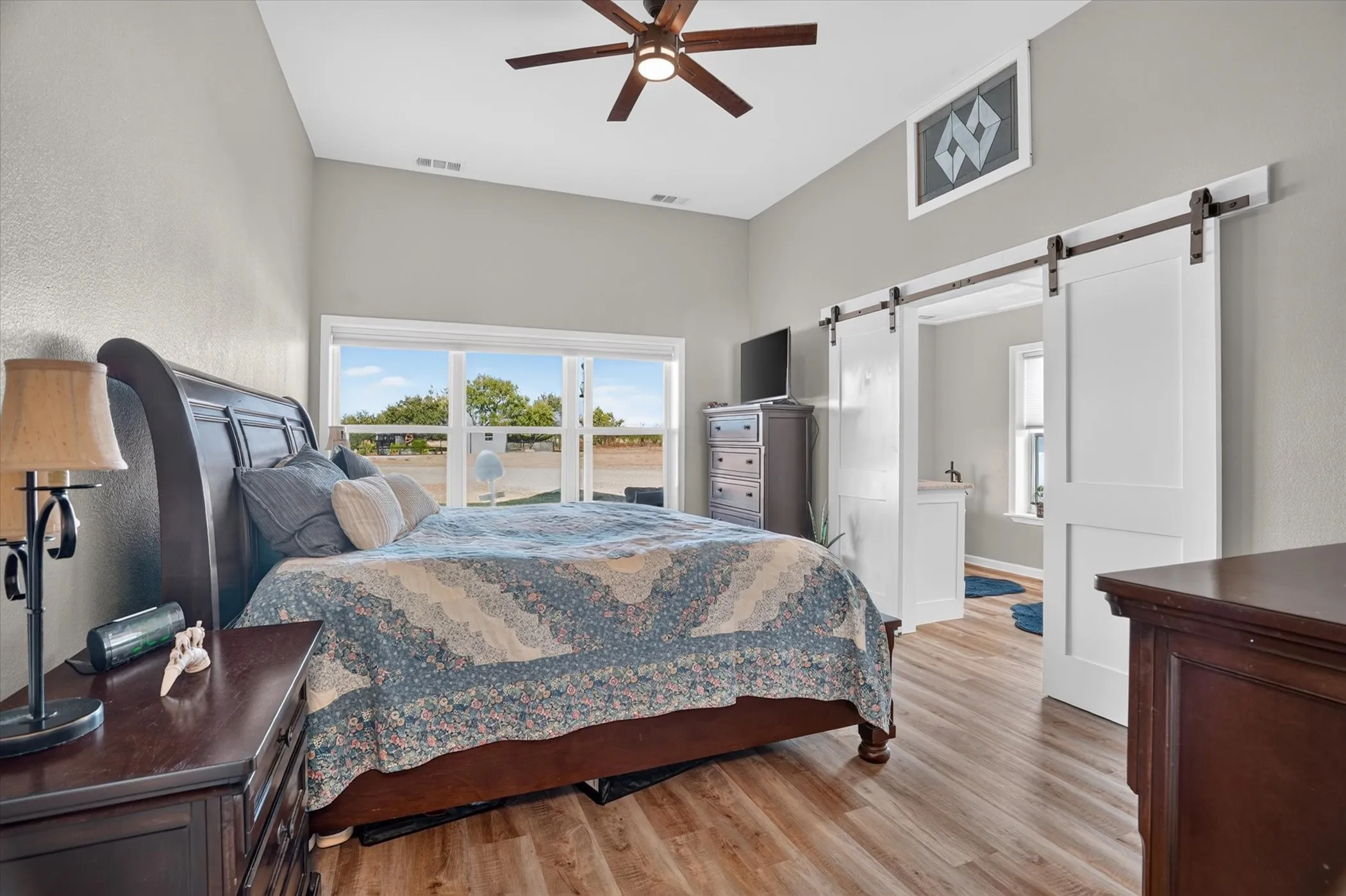 Vaulted ceiling with a ceiling fan, wood-finish flooring, expansive windows, and a sliding barn door entry