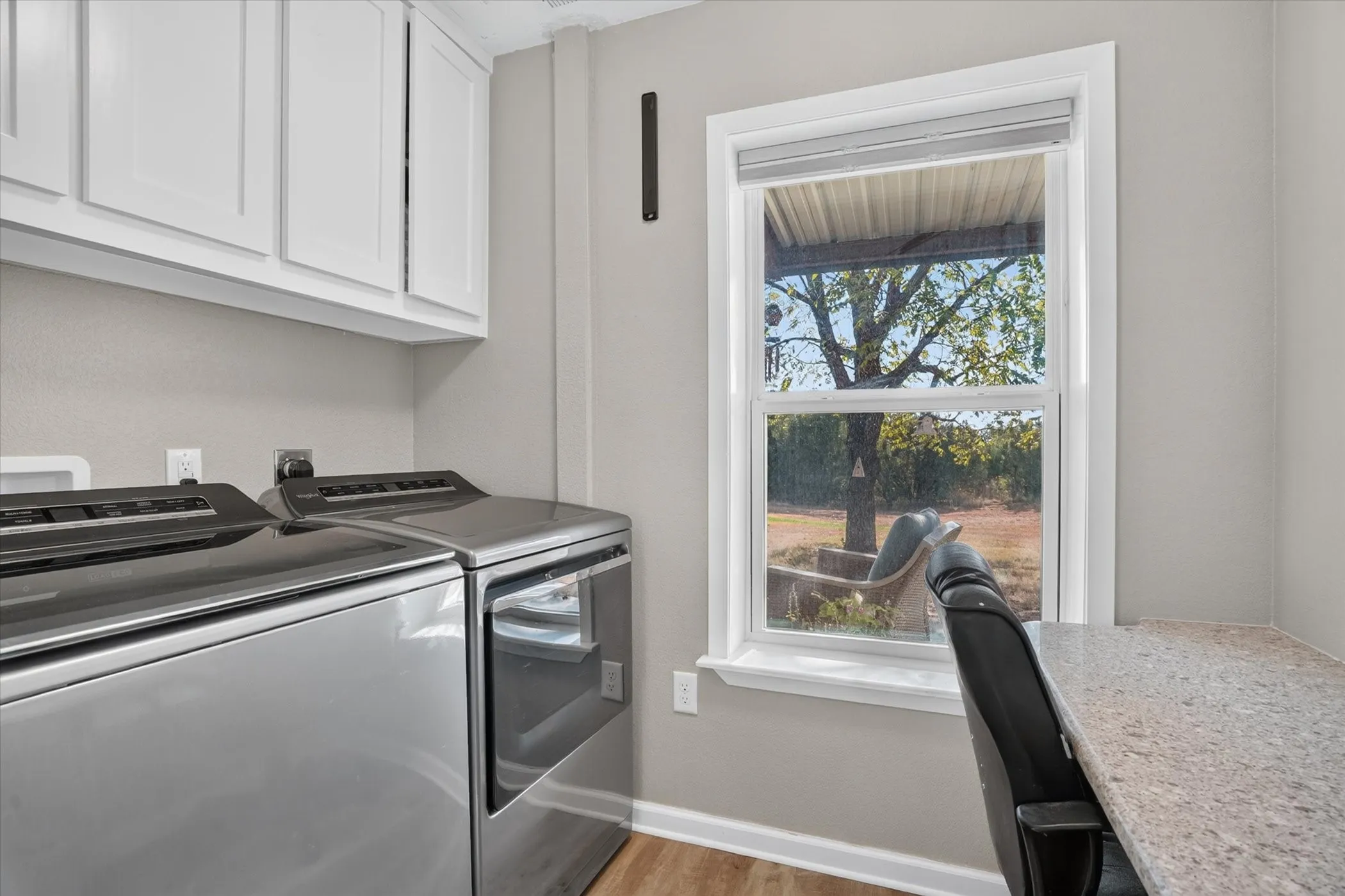 White upper cabinetry, wood-finish flooring, and a window with a roller shade