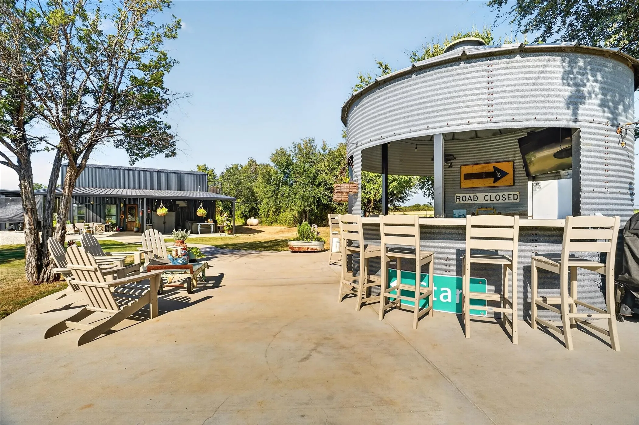 Concrete patio with a unique corrugated metal outdoor bar structure and a separate building featuring a metal roof