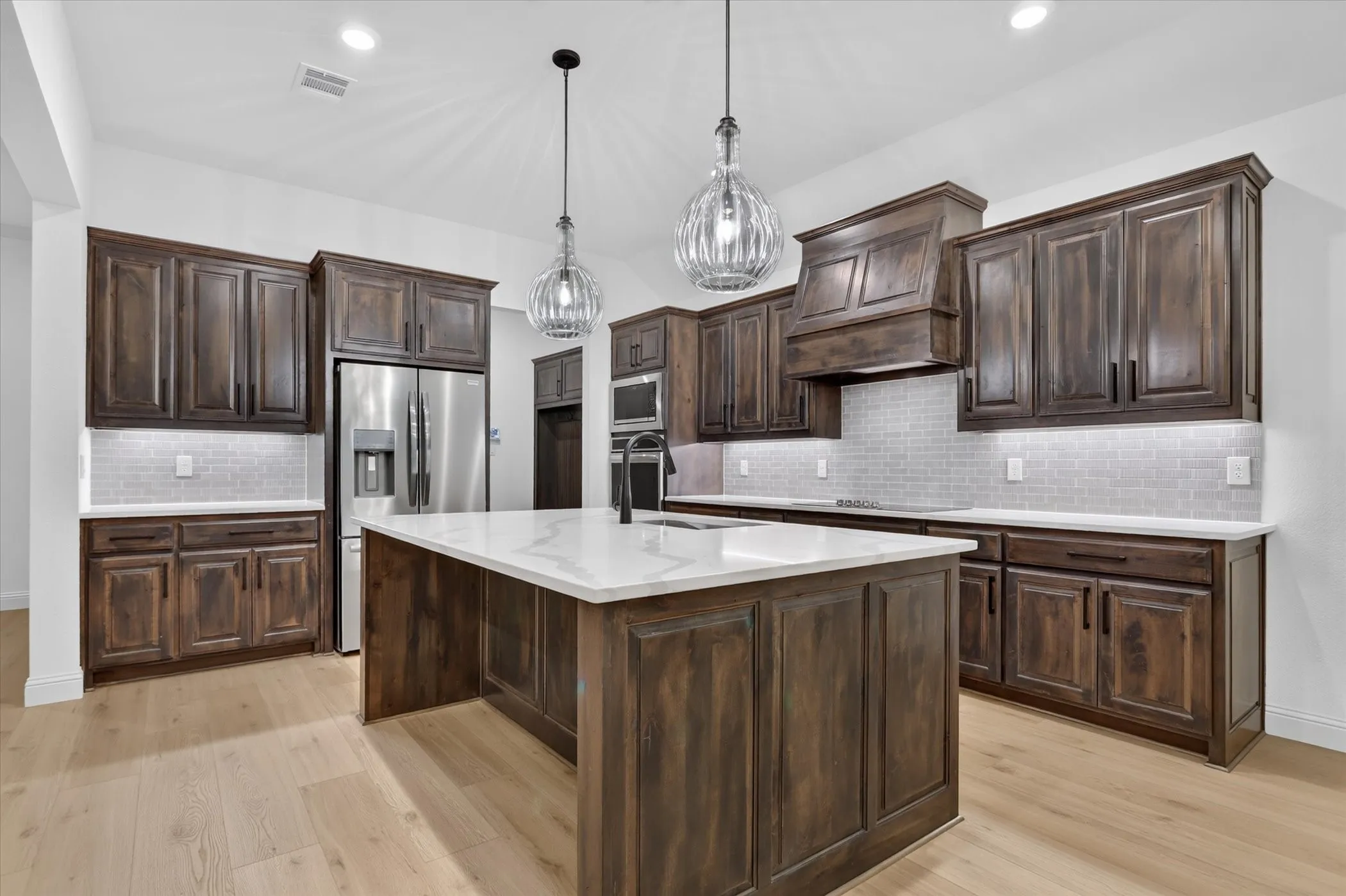 Kitchen featuring a center island, wood-finish cabinetry, stainless steel appliances, a tile backsplash, and light wood-finish flooring