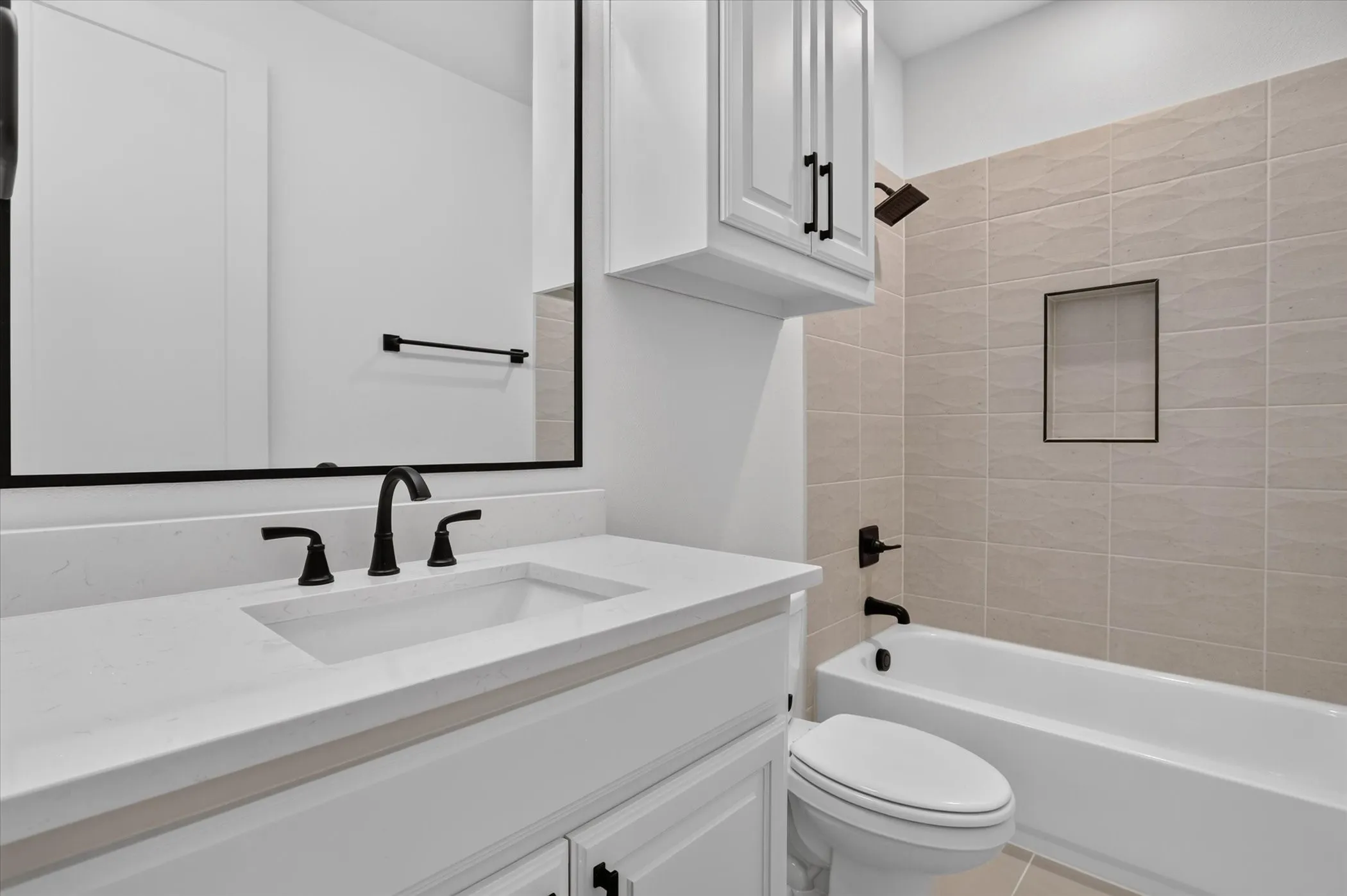 Bathroom featuring a single vanity with an undermount sink, a large framed mirror, matte black fixtures, a built-in bathtub, and tiled walls