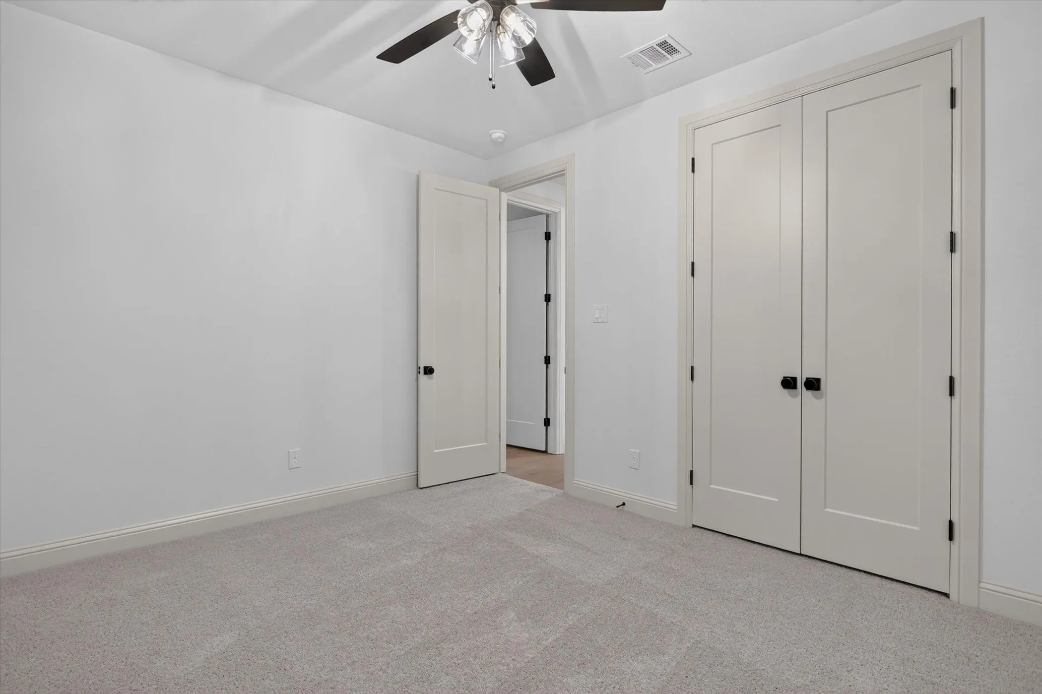 Plush carpeting, ceiling fan with light, modern doors with black hardware, and crisp white walls