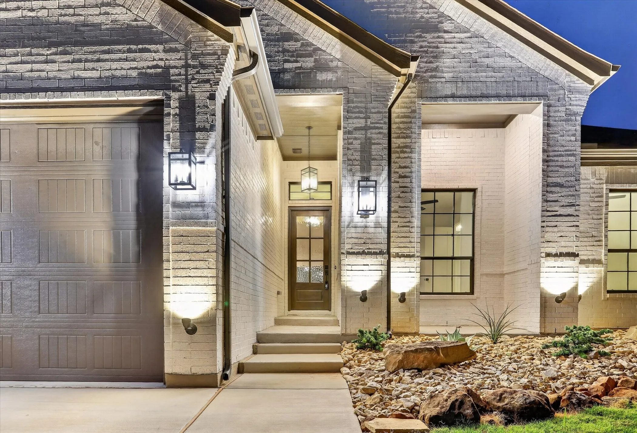 Modern brick exterior with clean architectural lines, featuring a welcoming front entry with dual wall sconces, multi-pane glass door, and recessed lighting