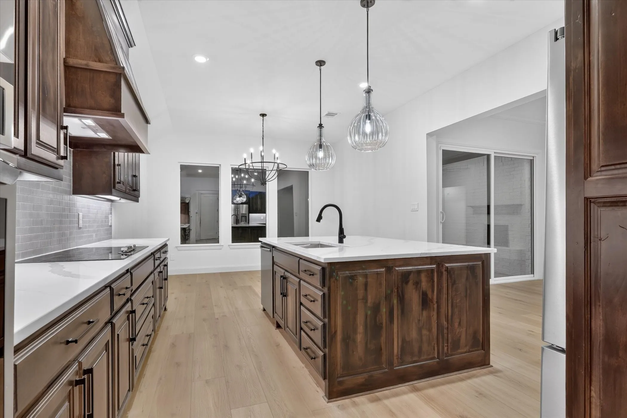 Gourmet kitchen featuring rich wood cabinetry, white quartz countertops, a substantial center island with storage, stainless steel appliances, pendant lighting, subway tile backsplash, and wide-plank wood-finish flooring throughout