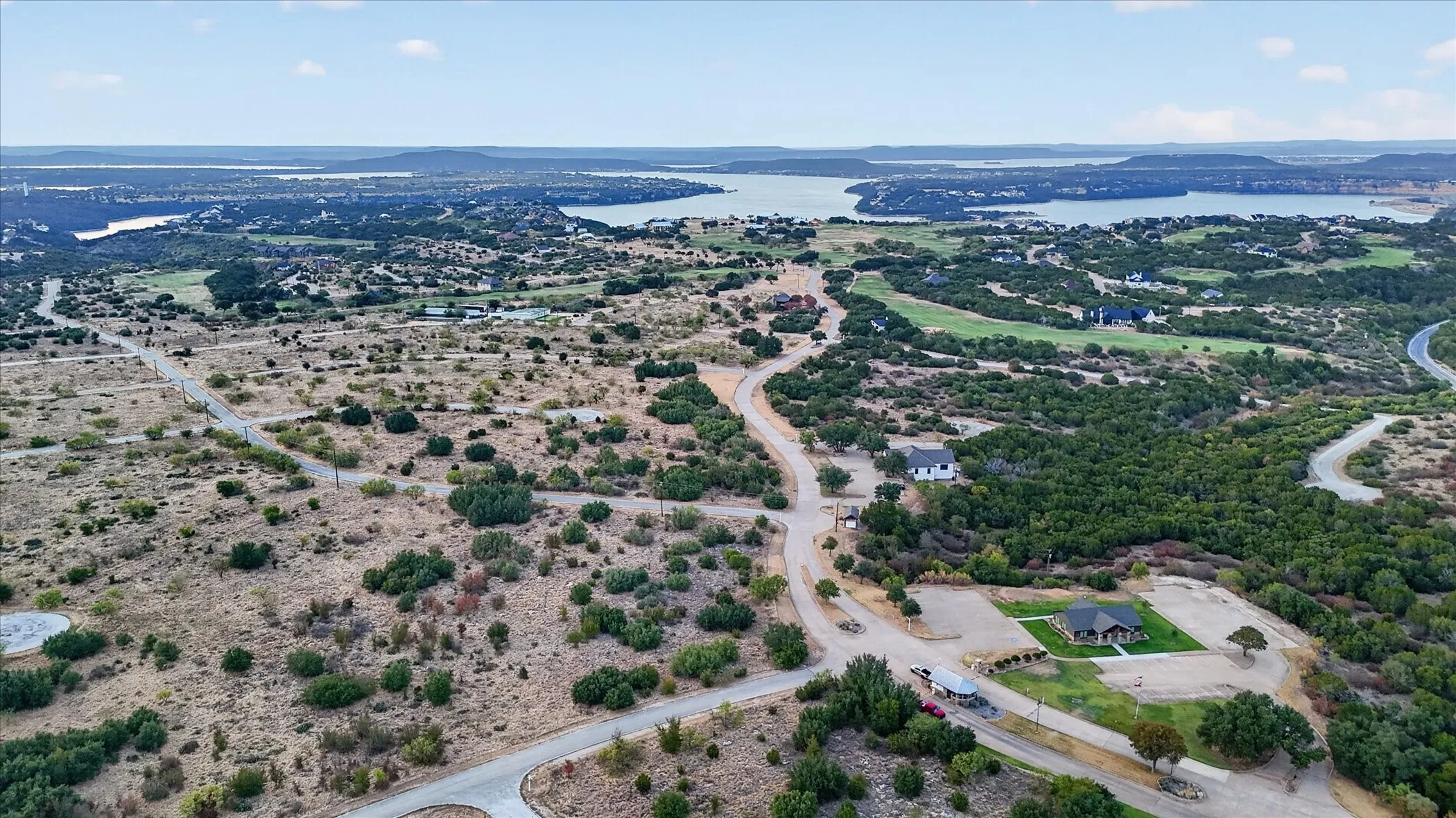 Expansive landscape featuring distant bodies of water, winding paved roads, and scattered residential properties