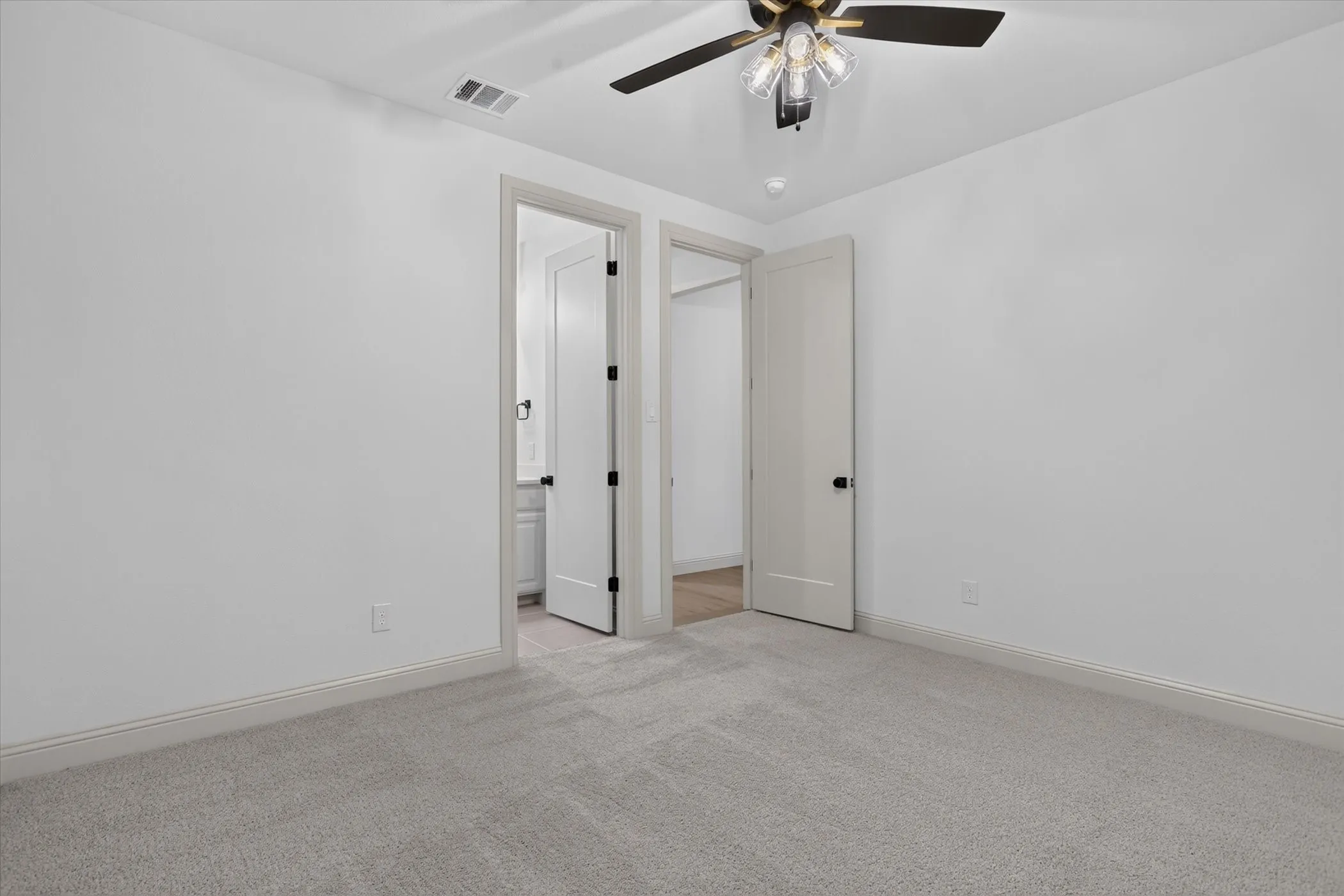 Light gray carpeted flooring, white painted walls, and a ceiling fan with integrated lighting