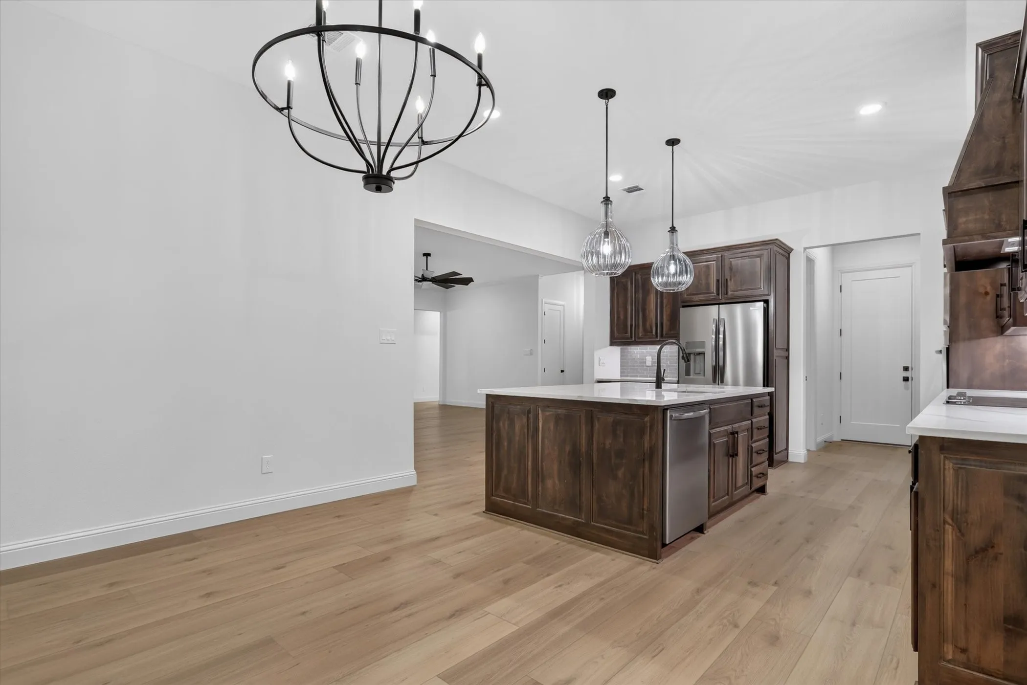 Spacious kitchen featuring an island with pendant lighting, wood-finish flooring, custom wood cabinetry, and stainless steel appliances