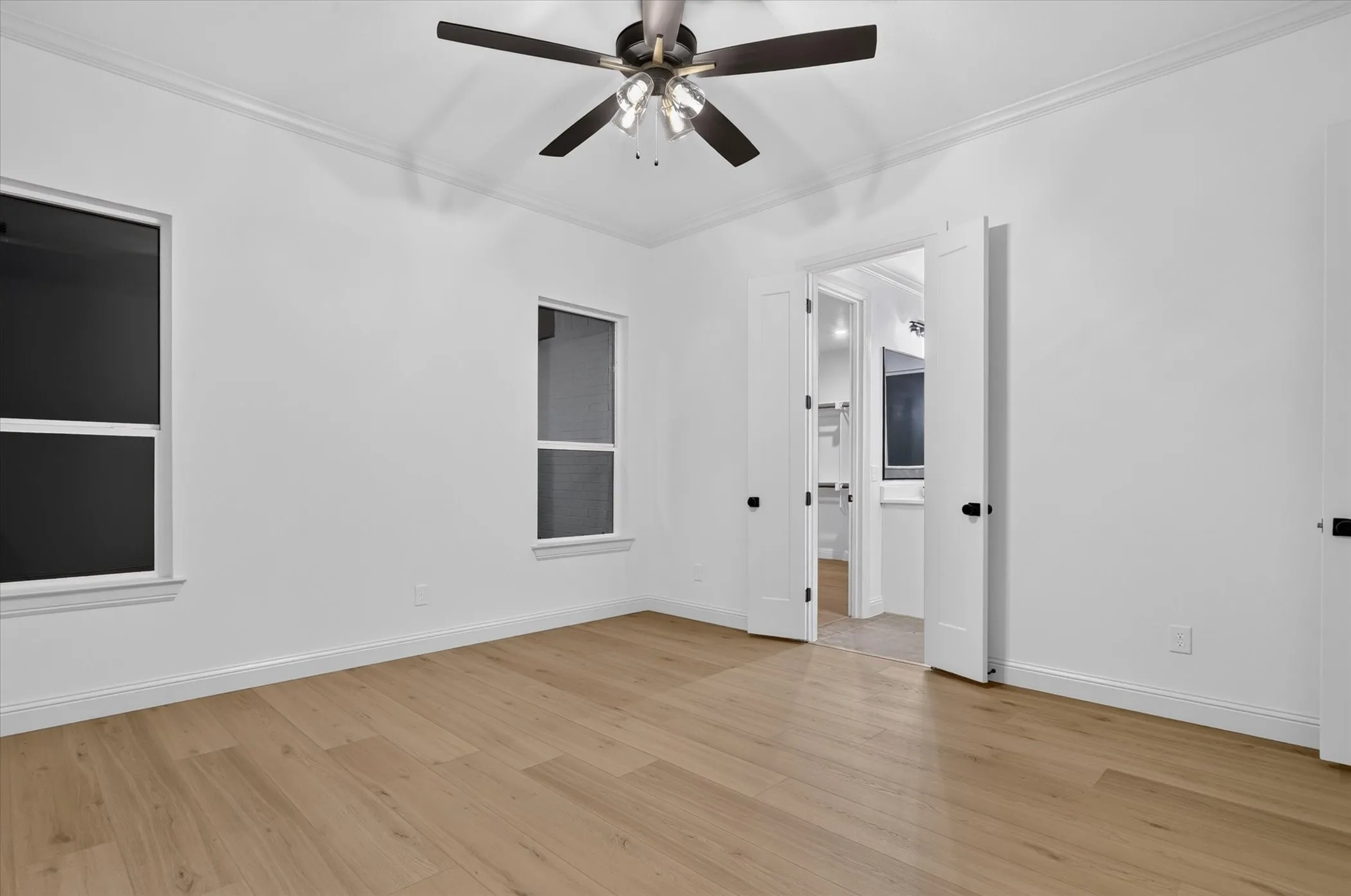Wood-finish flooring, white walls, two windows, crown molding, and a ceiling fan with integrated lighting