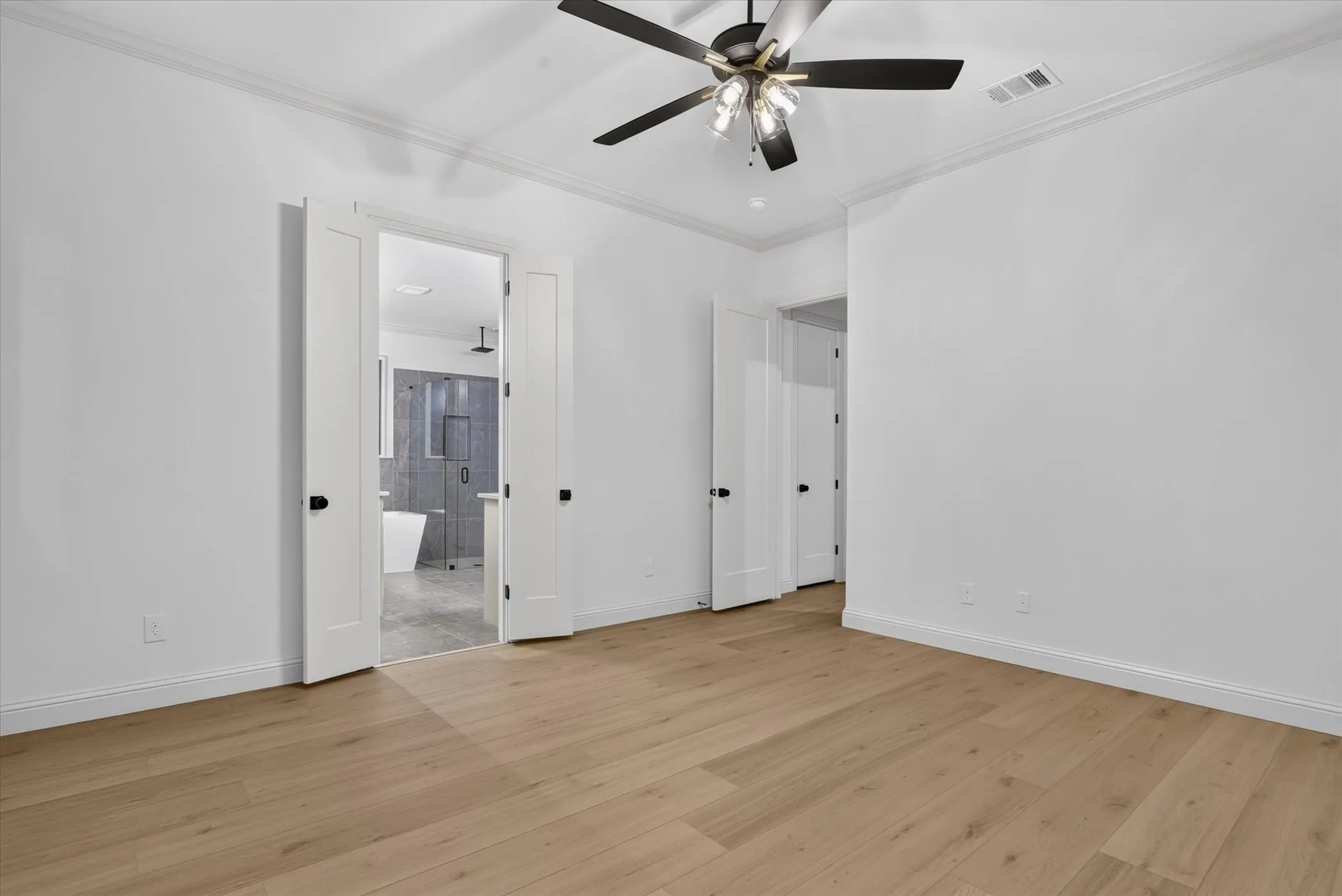Light wood-finish flooring, white walls, black ceiling fan, white double doors, and crown molding