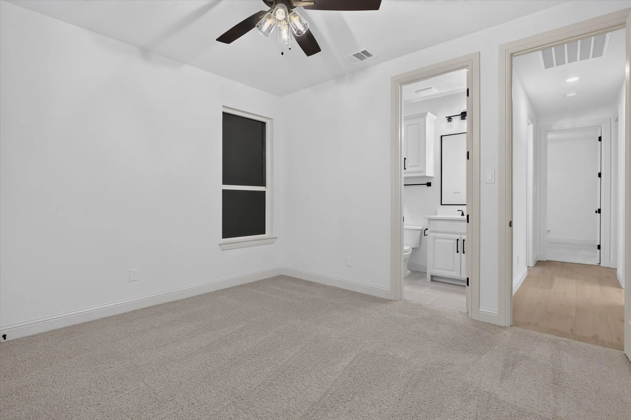 Recessed window, ceiling fan, carpeting, wood-finish flooring in hallway, bathroom with vanity and toilet
