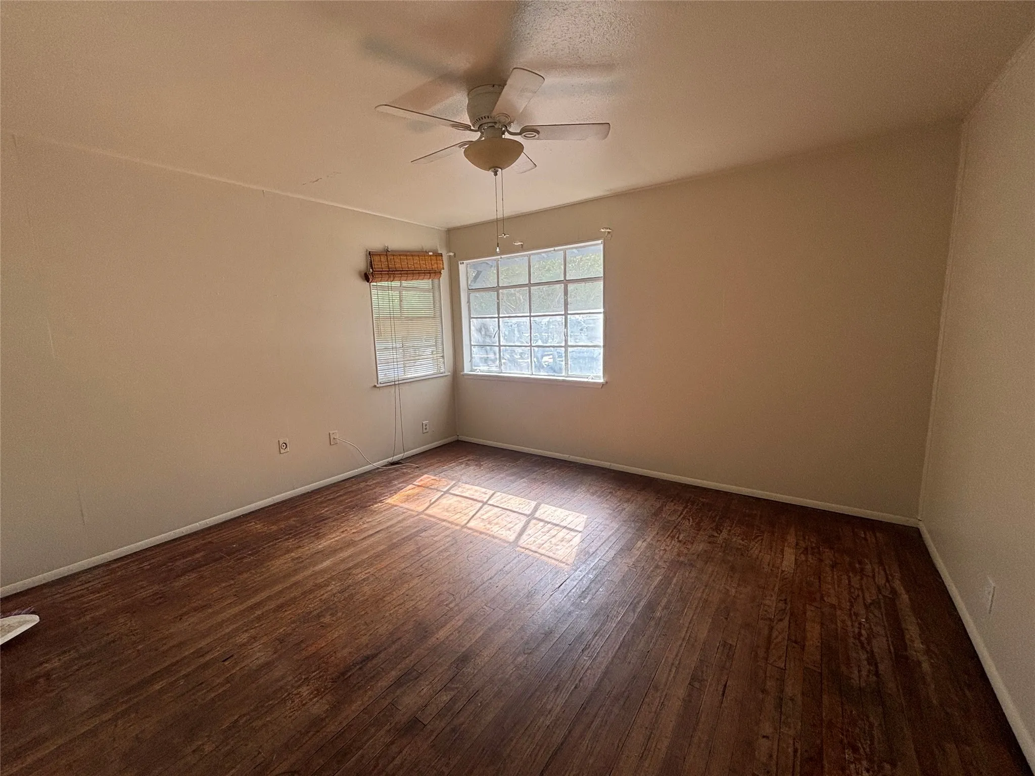 Wood-finish flooring with a ceiling fan light fixture and two windows