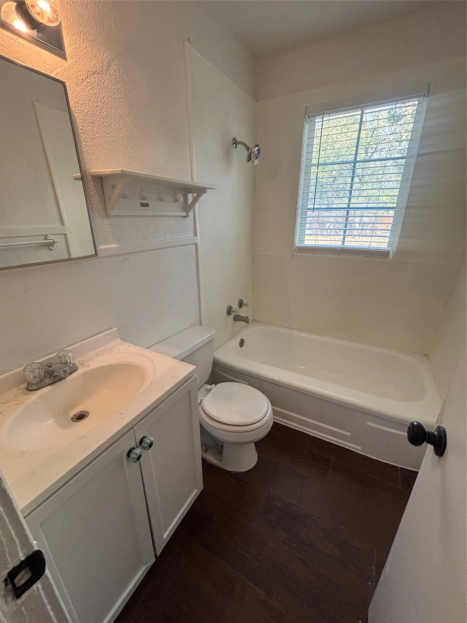 White vanity with a single basin sink, wood-finish flooring, and a window with blinds