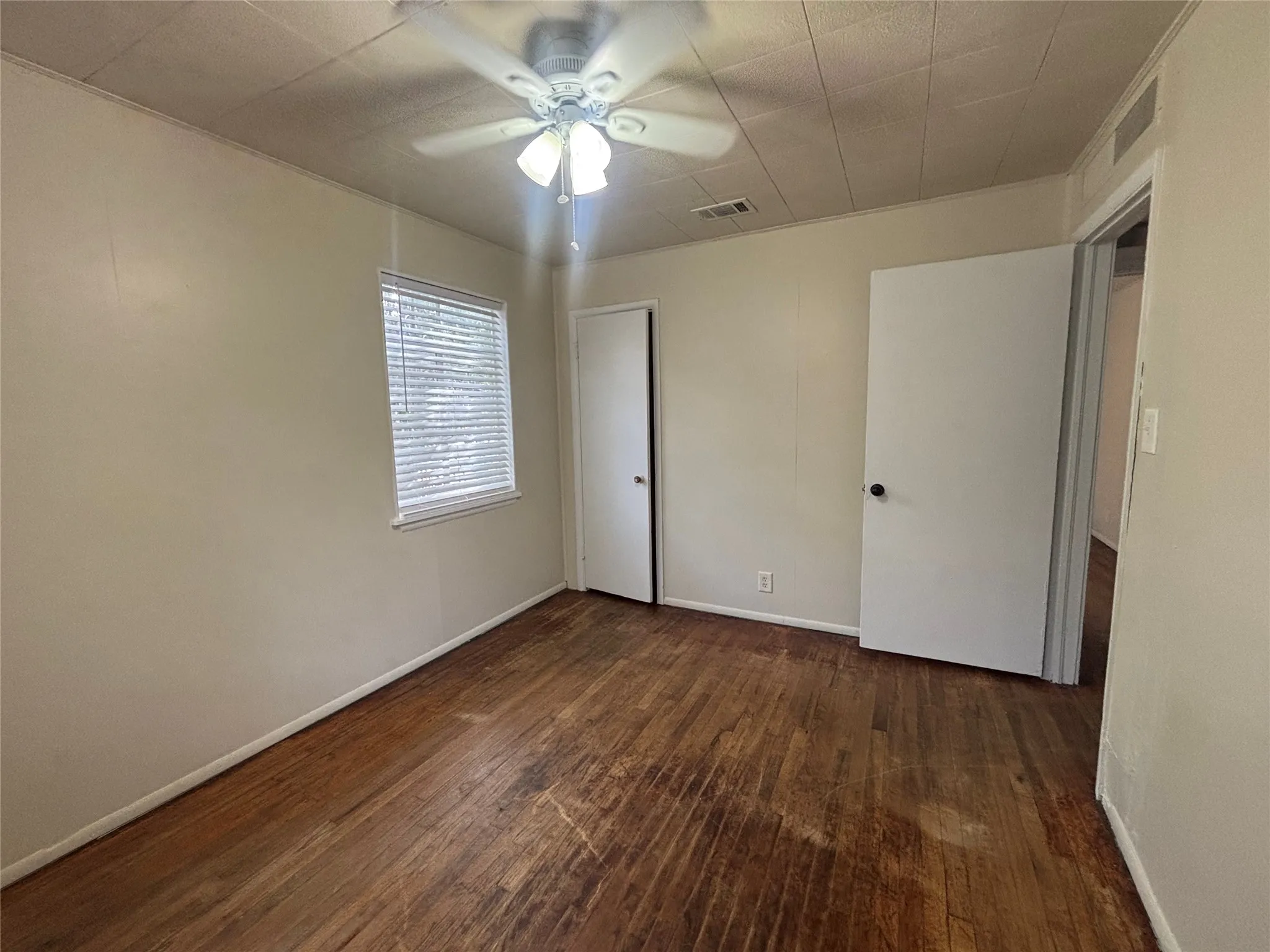 Wood-finish flooring, ceiling fan with integrated lighting, window with blinds, and white interior doors