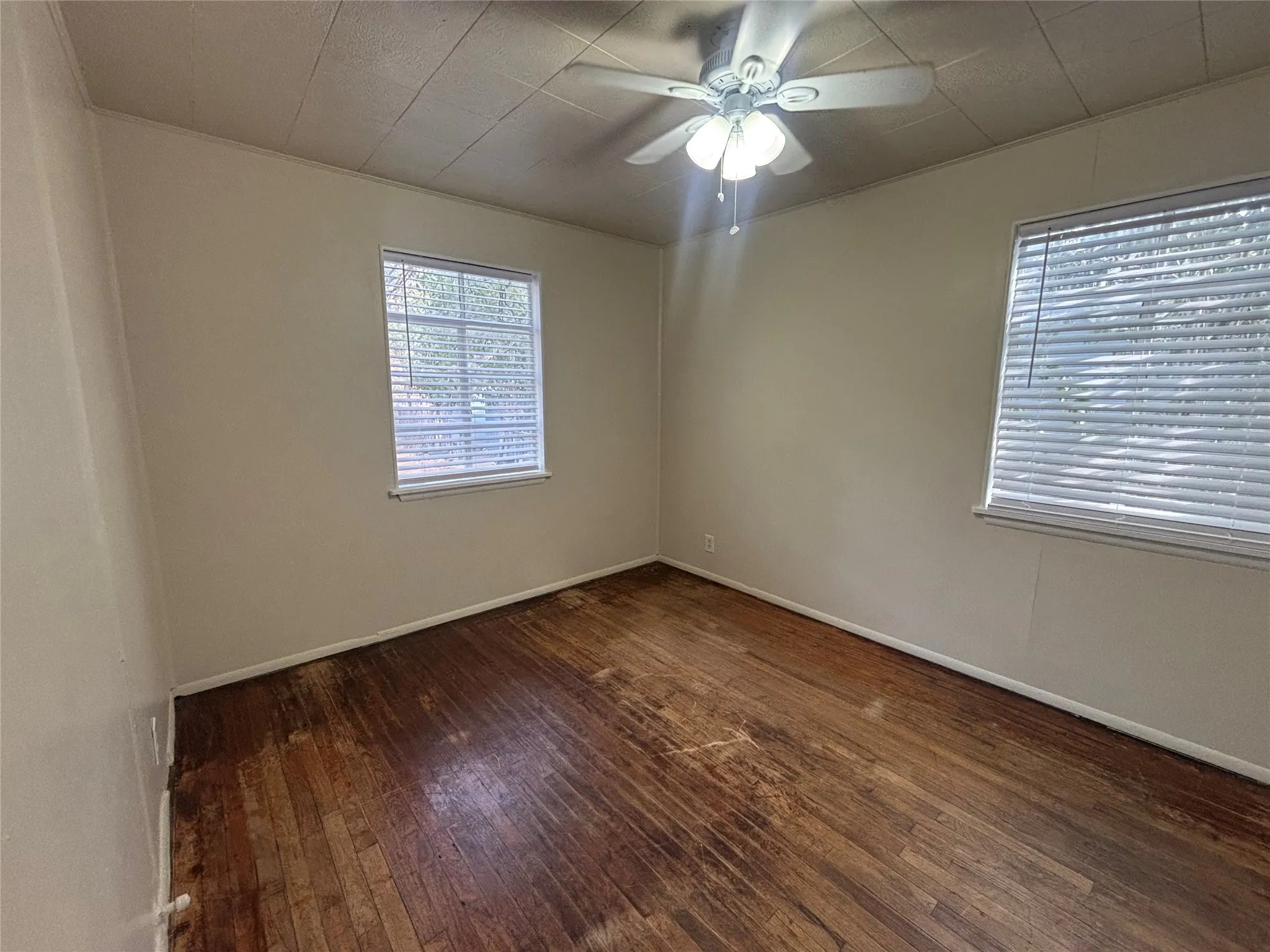 Wood-finish flooring, two windows with blinds, ceiling fan with integrated lighting, and neutral wall paint