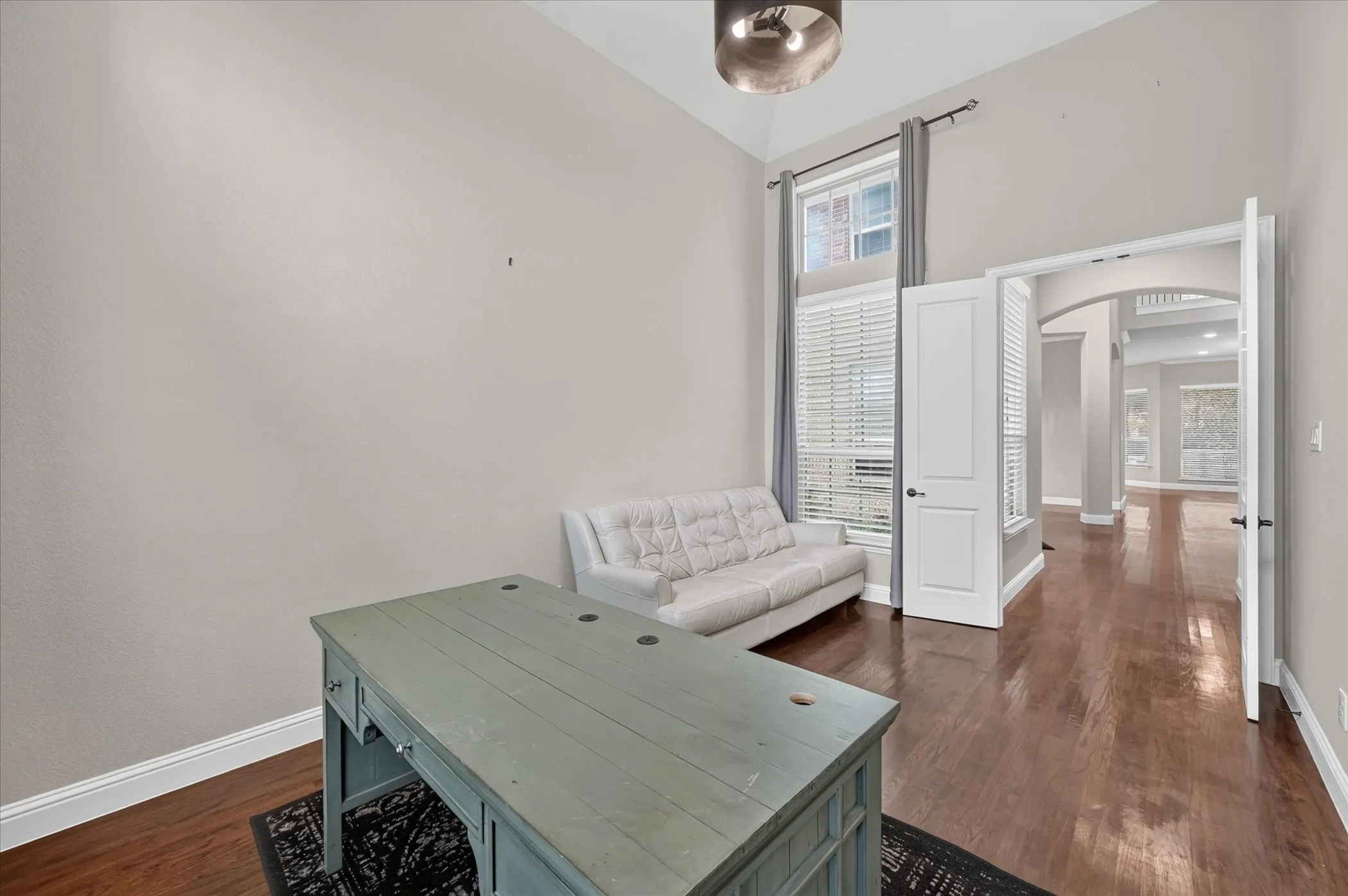 Bright office or den featuring hardwood flooring, abundant natural light from large windows with plantation shutters, and a light gray painted accent wall