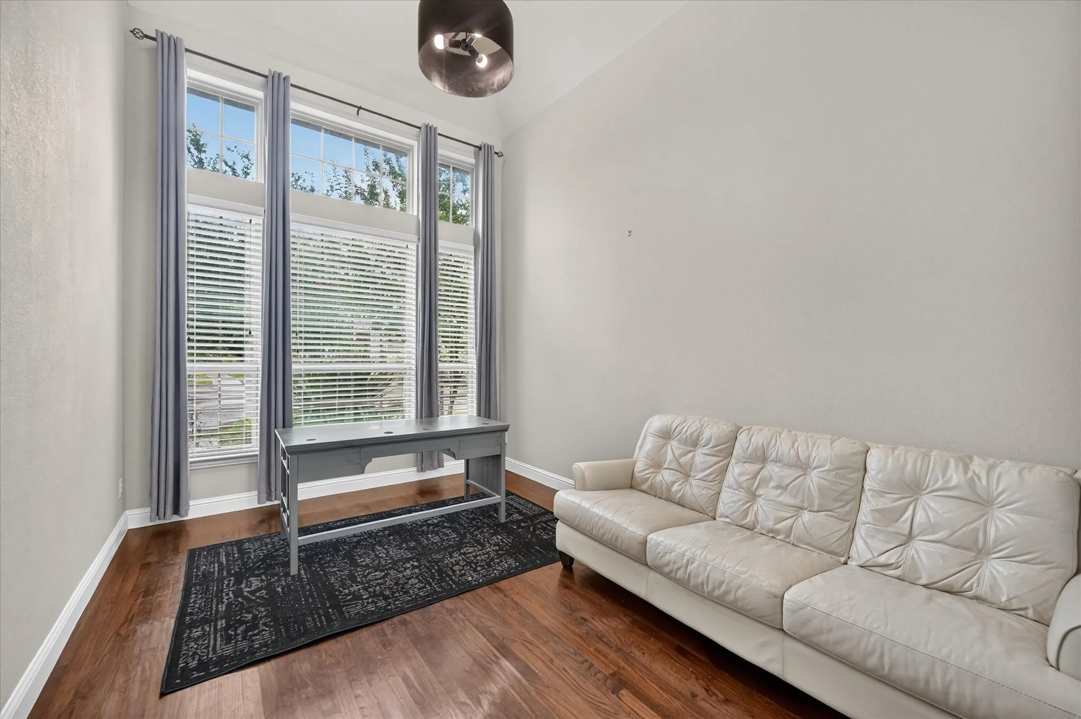 Vaulted ceiling, three tall windows with blinds, wood-finish flooring, and a contemporary ceiling light fixture