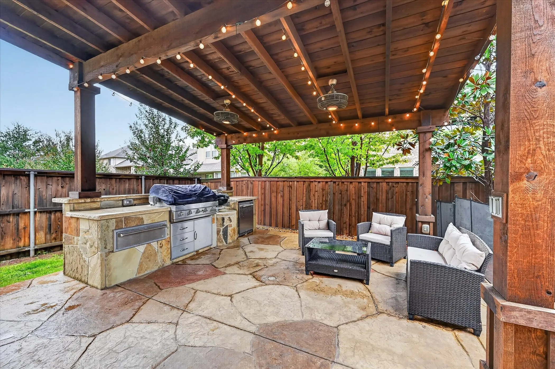 Expansive covered patio featuring a built-in stone outdoor kitchen, irregular flagstone paving, and a wood plank ceiling