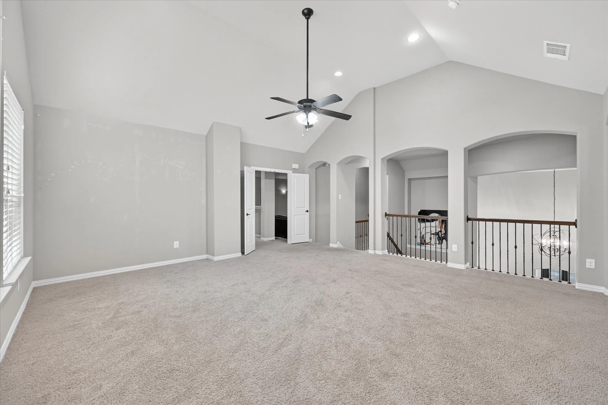 Vaulted ceiling with a ceiling fan, arched openings, wrought iron railings, and neutral carpeting