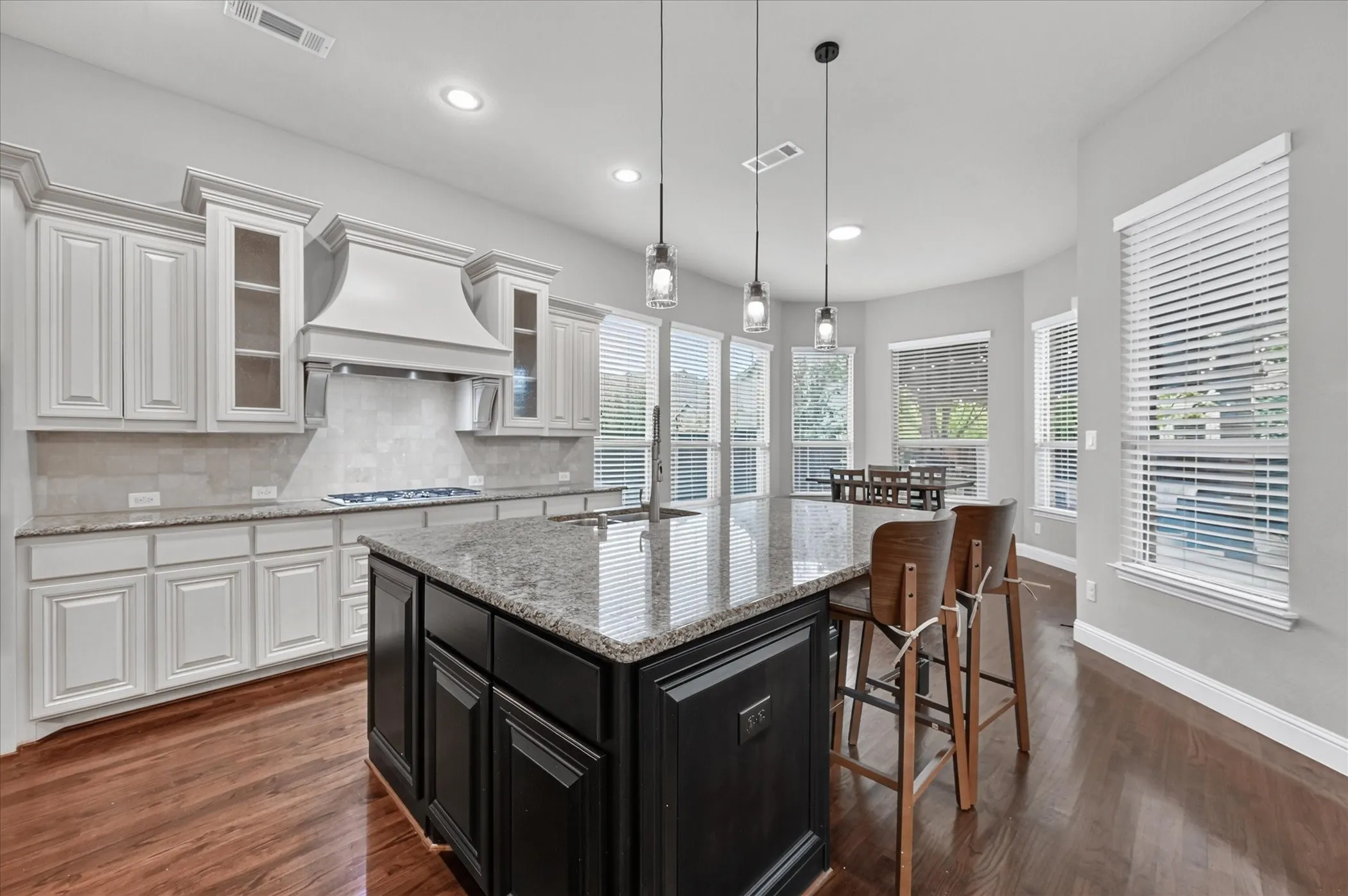 Gourmet kitchen featuring a large central island, white cabinetry, integrated range hood, tile backsplash, and wood-finish flooring