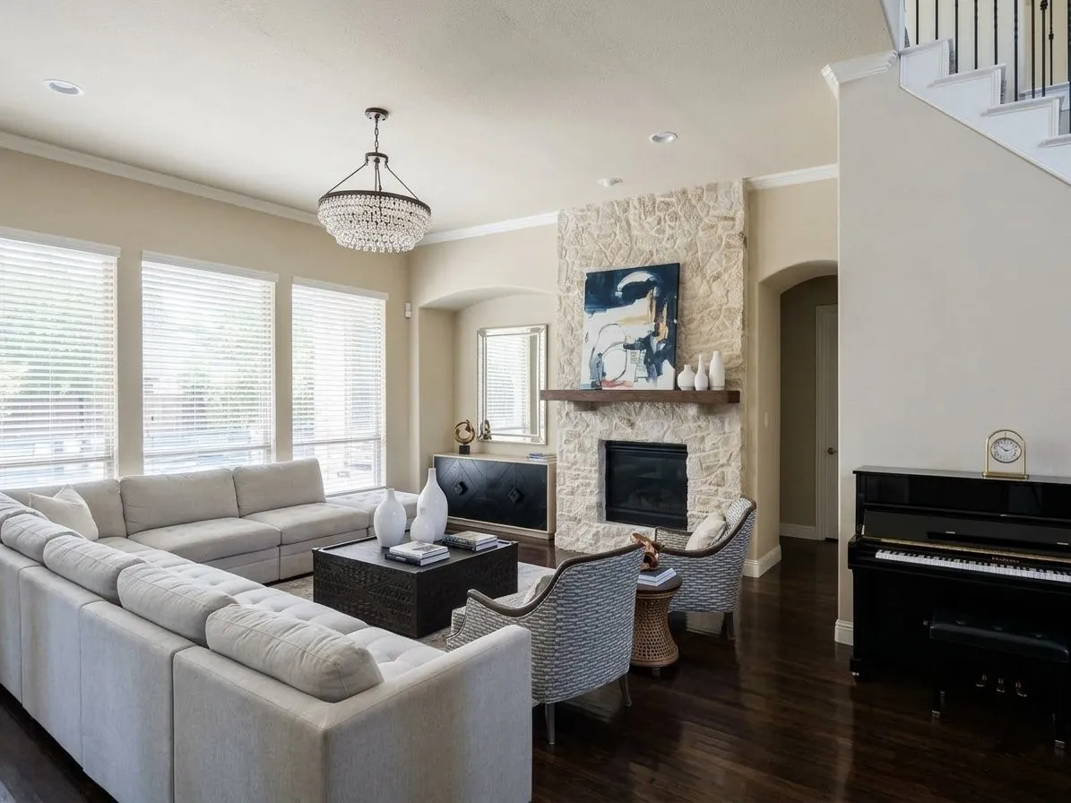 Spacious living area featuring dark wood-finish flooring, a stone-clad fireplace with a wood mantle, a decorative chandelier, recessed lighting, and a staircase with wrought iron balusters