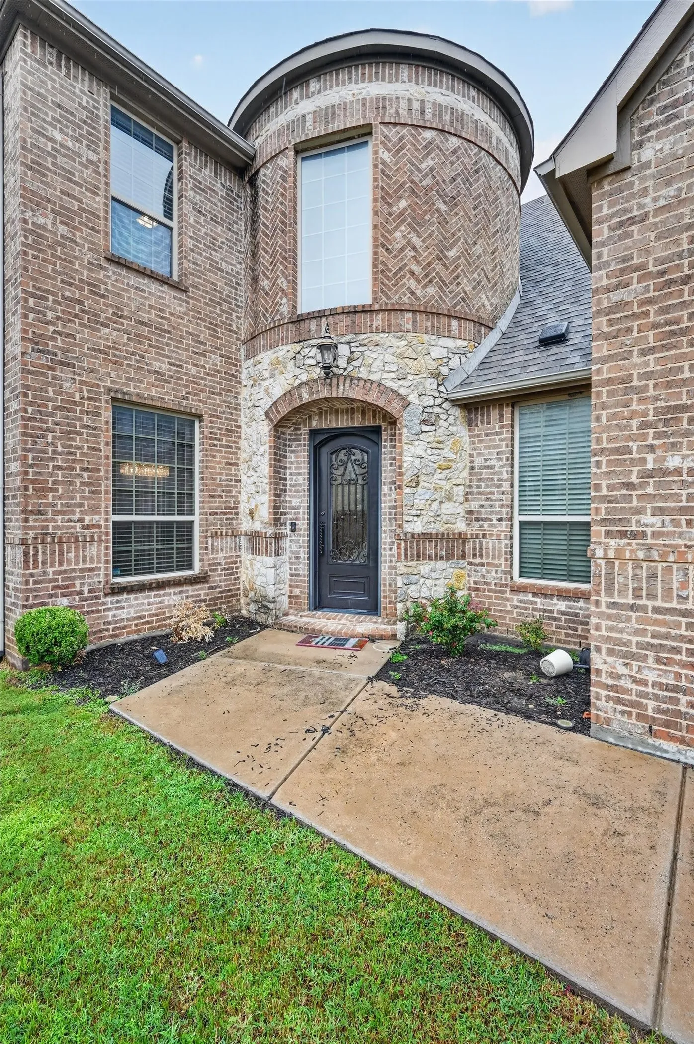 Brick facade with stone accents, arched entryway, and a prominent round tower feature with a large window