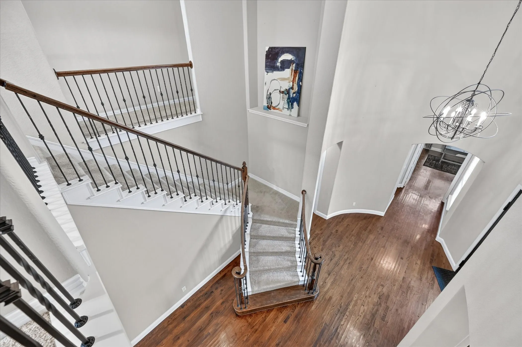 Grand entryway featuring a double staircase with wrought iron balusters and wood handrails, hardwood flooring, and a contemporary chandelier