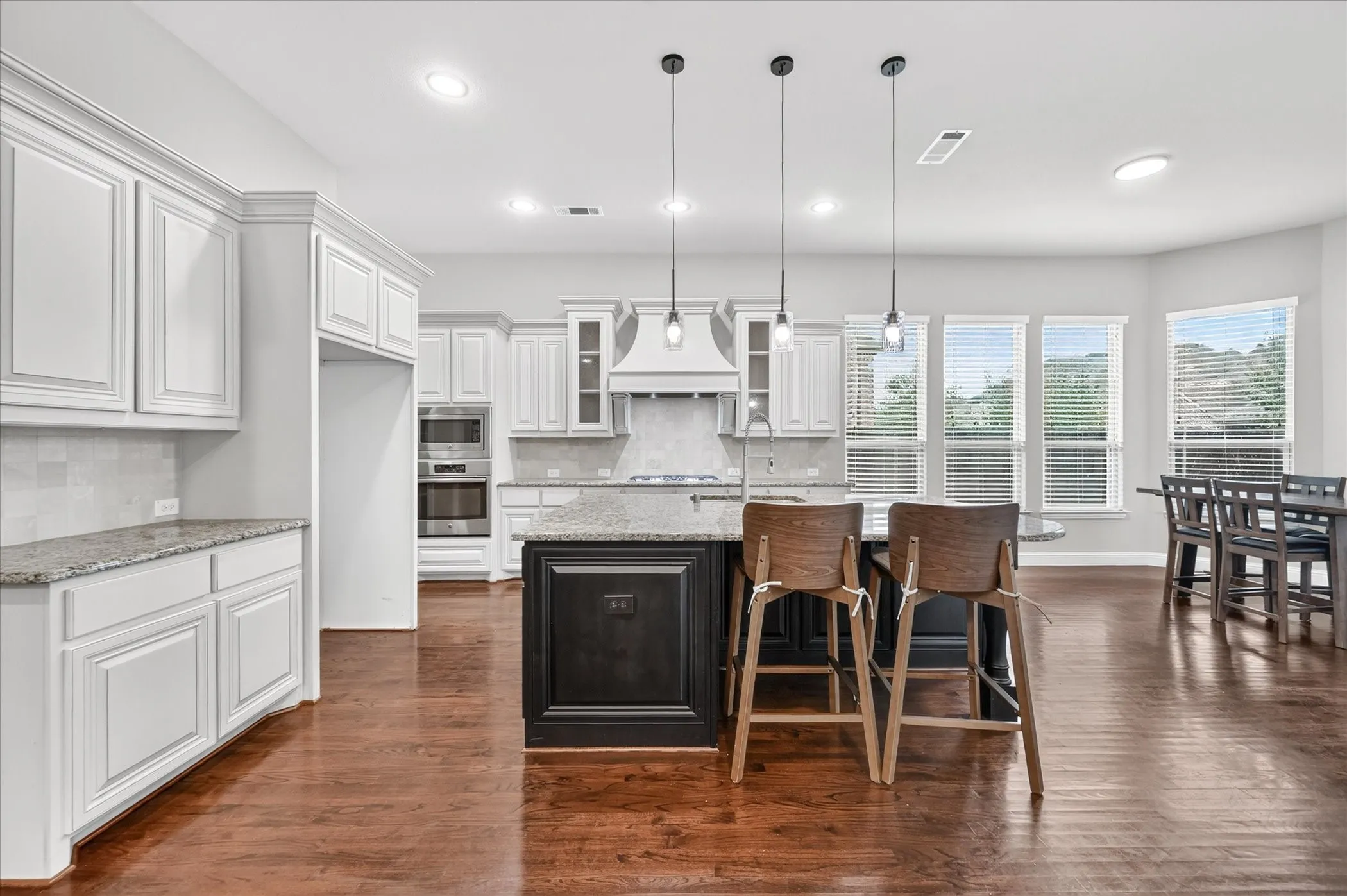Gourmet kitchen featuring a large island, wood-finish flooring, white cabinetry, granite countertops, and stainless steel appliances