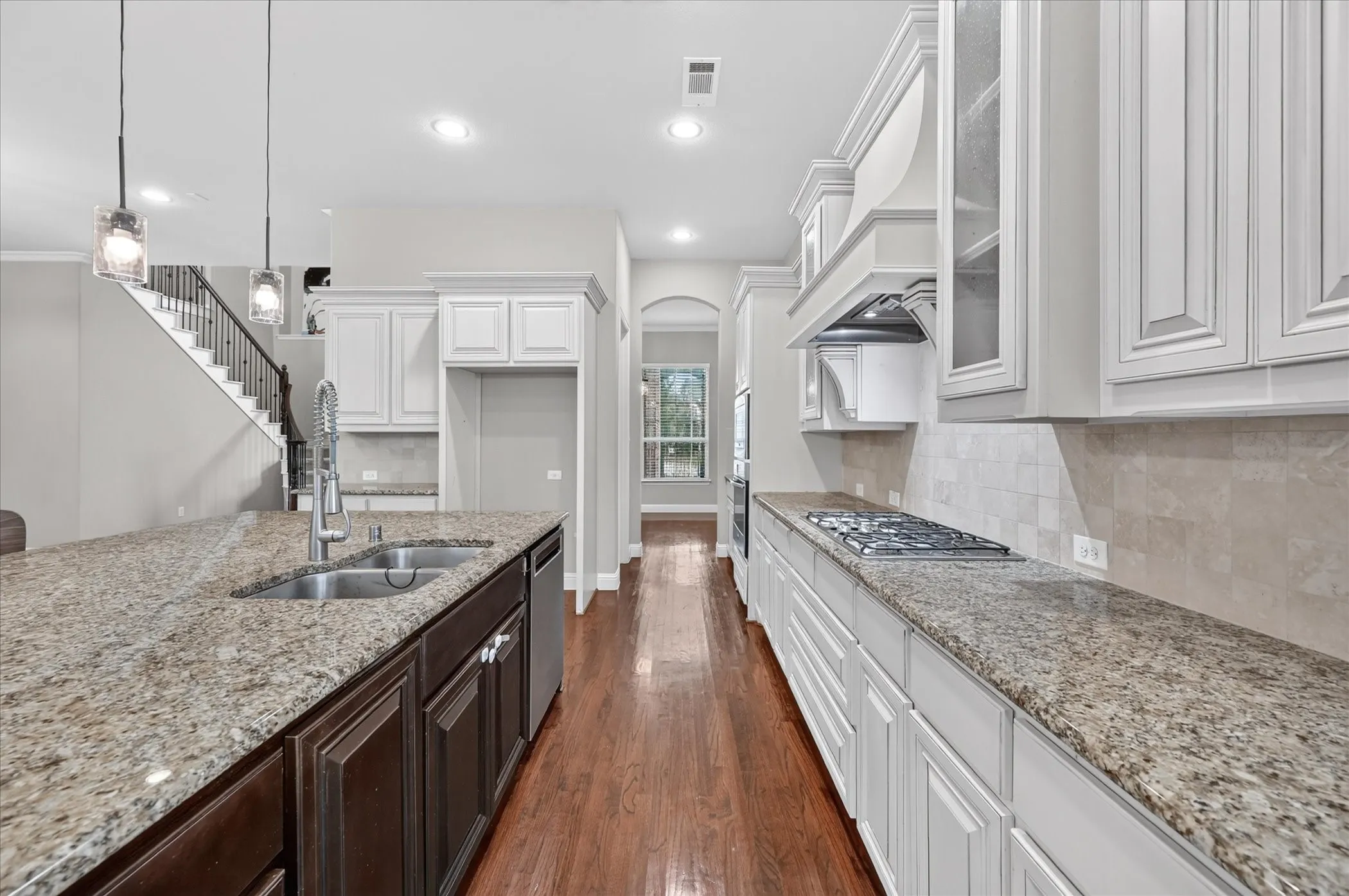 Spacious kitchen featuring granite countertops, wood-finish flooring, white cabinetry, a built-in gas range, and a double-basin sink
