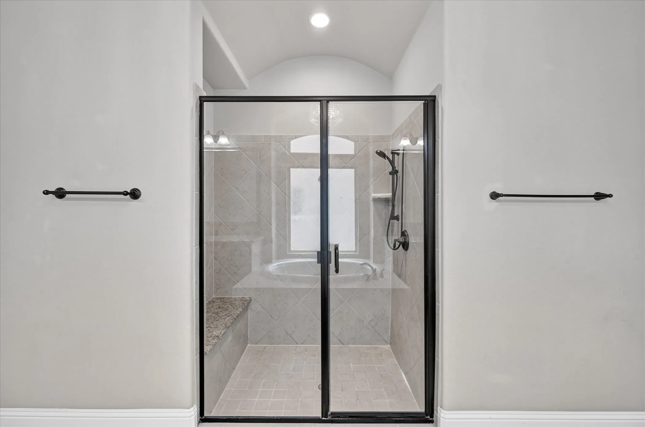 Enclosed shower with a glass door, tile flooring, built-in bench, and a standalone tub