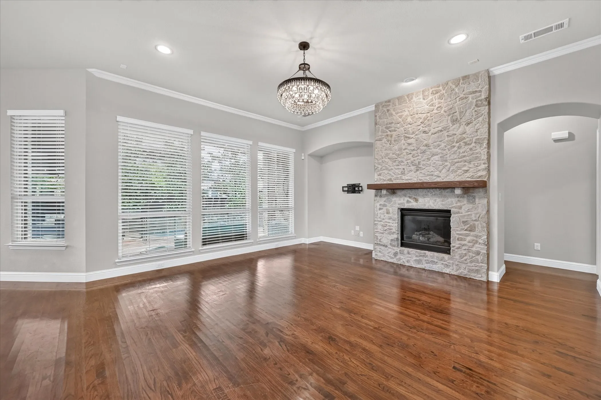 Stone-clad fireplace with wood mantel, rich wood-finish flooring, and crown molding