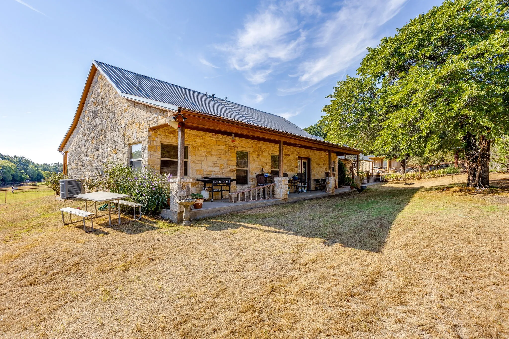 Stone exterior with a metal roof, extended covered porch, and mature trees