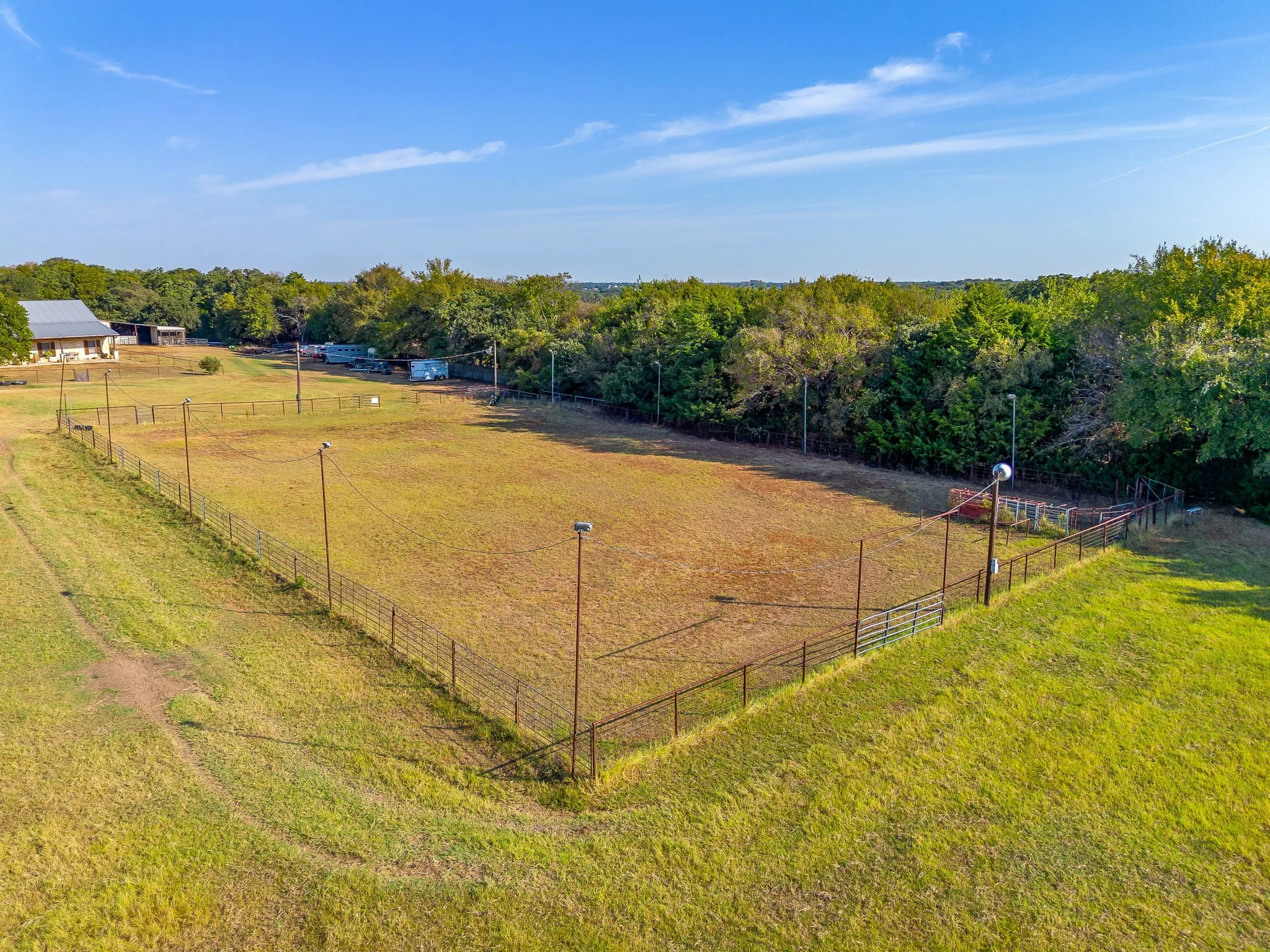 Fenced property with extensive grassy areas, tree-lined perimeter, and a distant outbuilding