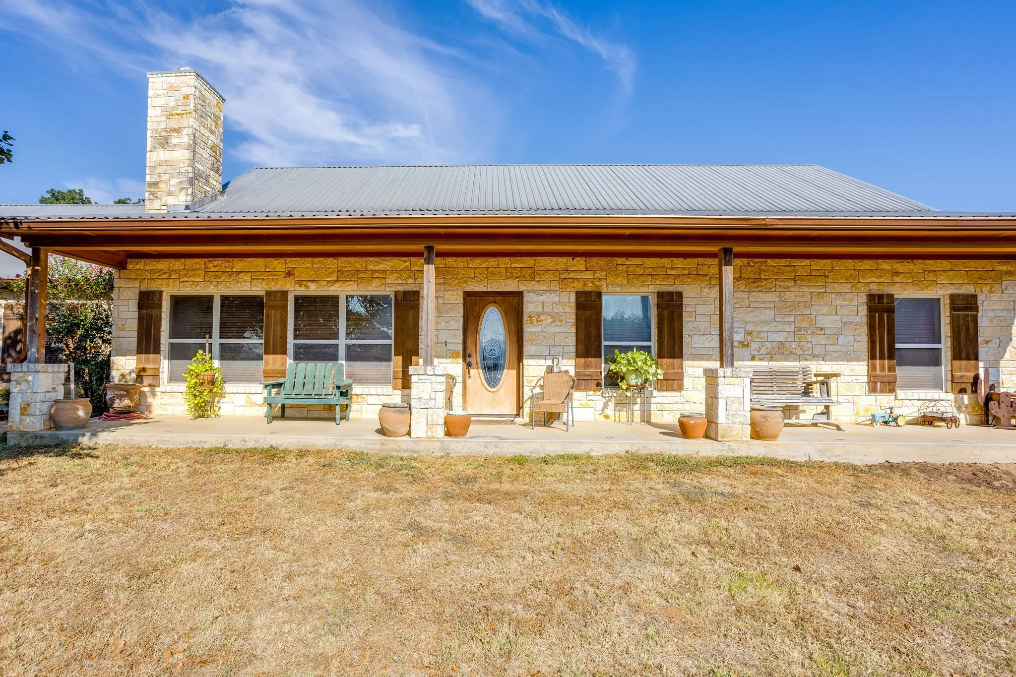 Stone veneer exterior with a metal roof, prominent stone chimney, and a full-length covered porch