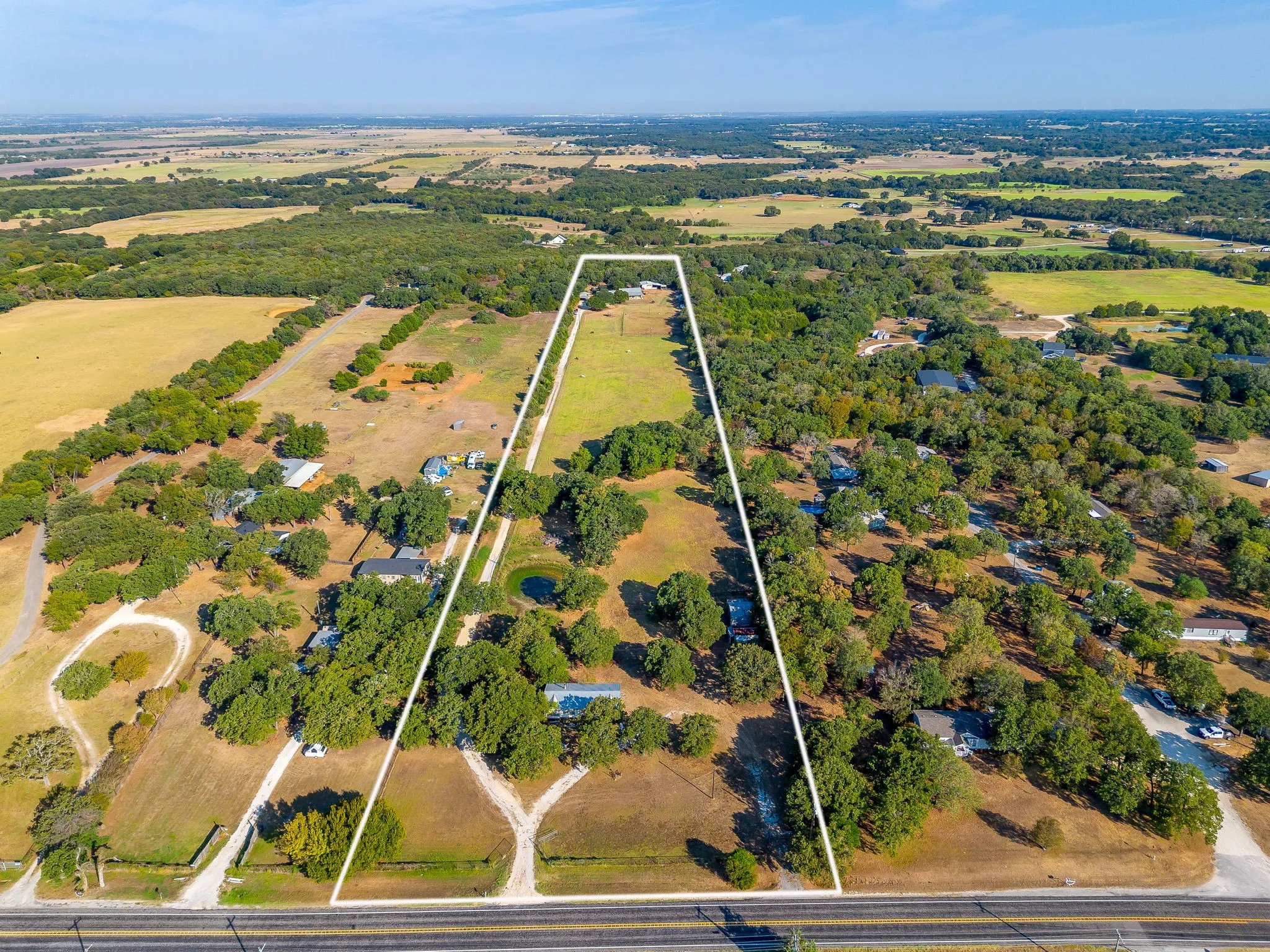 Expansive rural acreage featuring a natural pond, mature trees, and direct road frontage