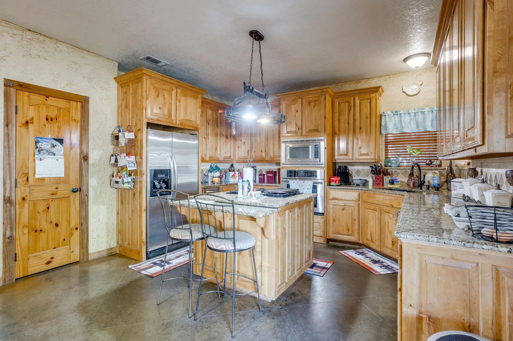 Kitchen featuring wood-finish cabinetry, granite-finish countertops, a central island with seating, stainless steel appliances, and concrete-finish flooring