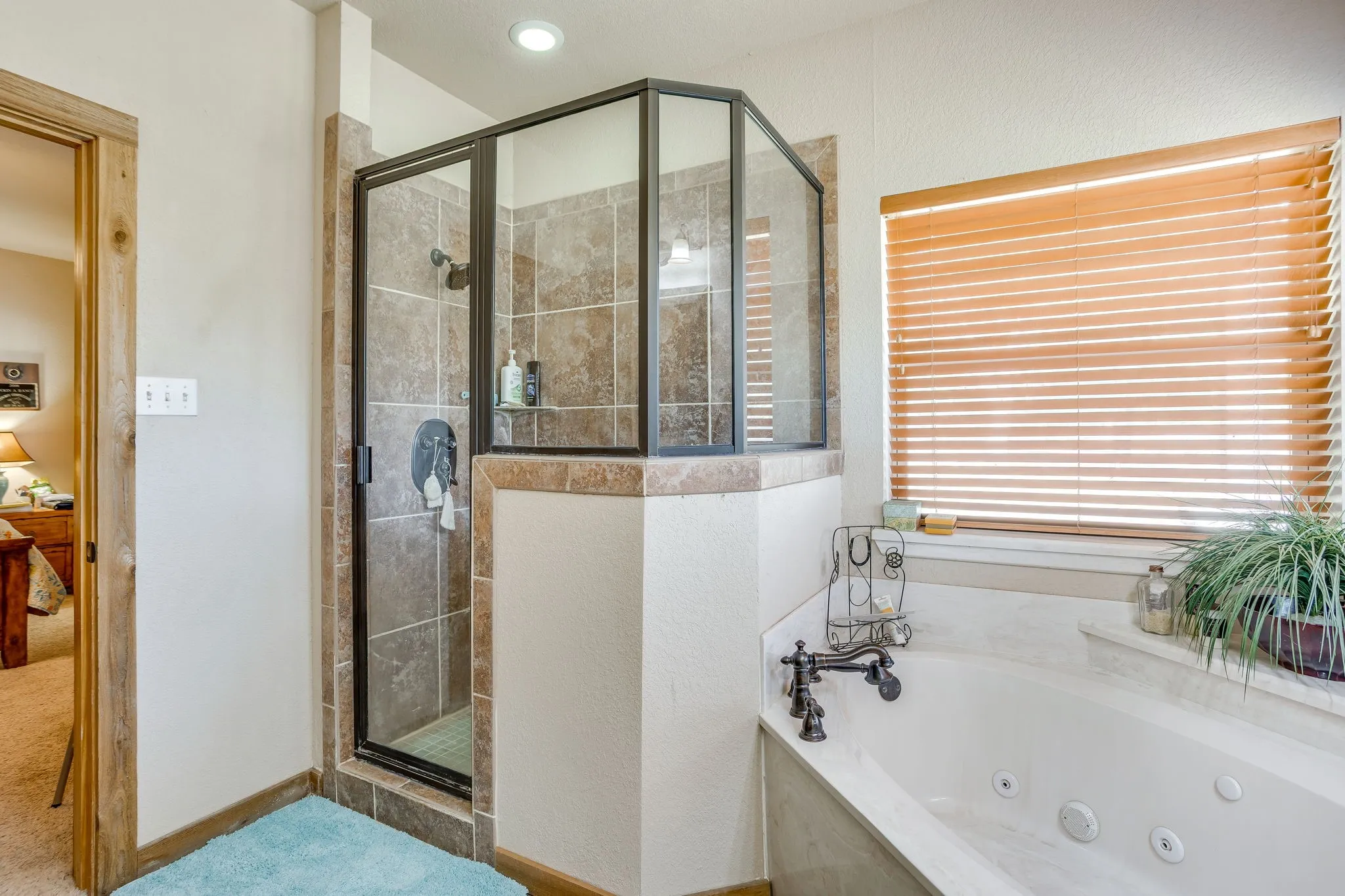 Tiled walk-in shower with a glass enclosure, jetted soaking tub, and natural wood window blinds