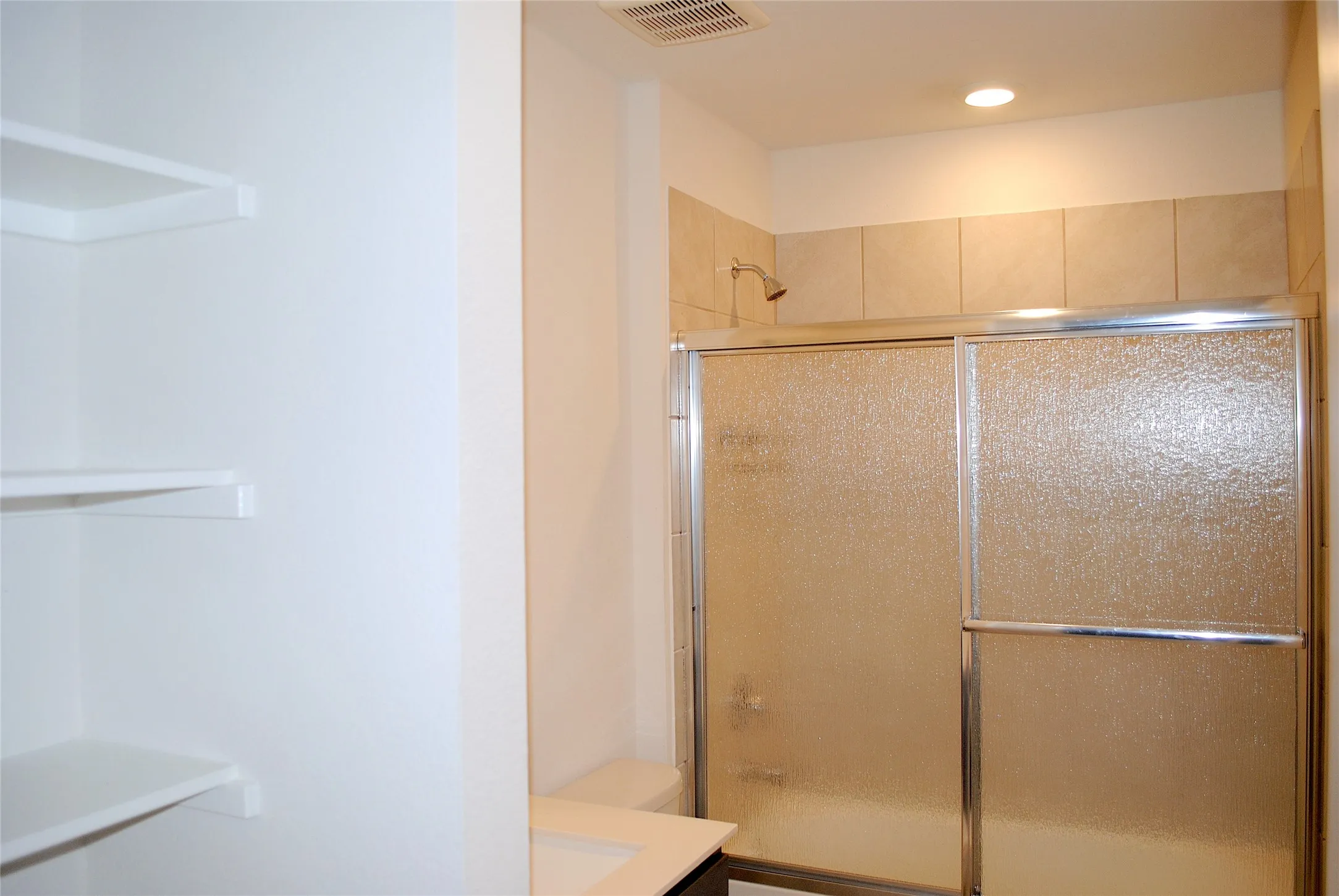 Shower with textured glass sliding doors, neutral tile surround, recessed lighting, and built-in shelving
