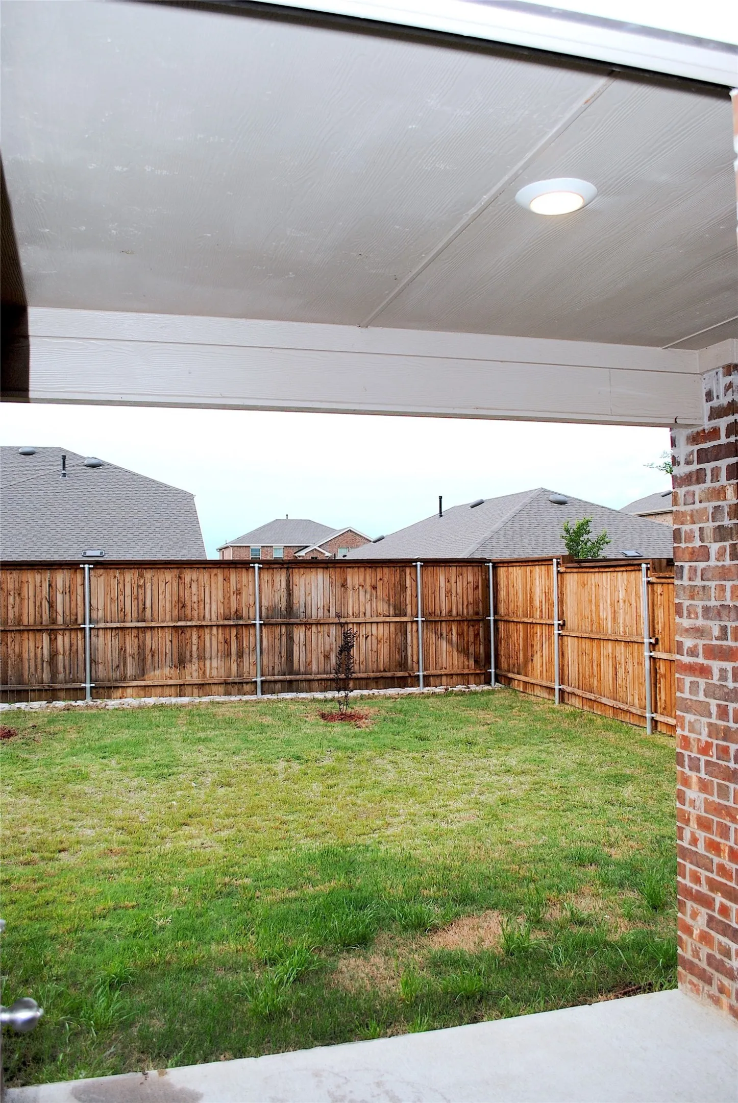 Covered patio with recessed lighting, brick pillar, concrete flooring, and a fully fenced backyard with a grass lawn