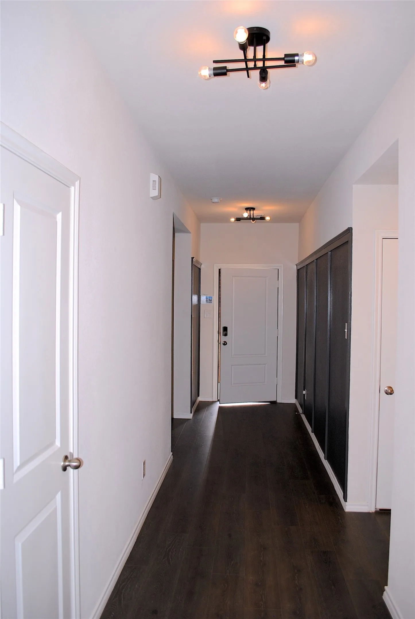 Hallway featuring wood-finish flooring, white walls, and contemporary ceiling light fixtures